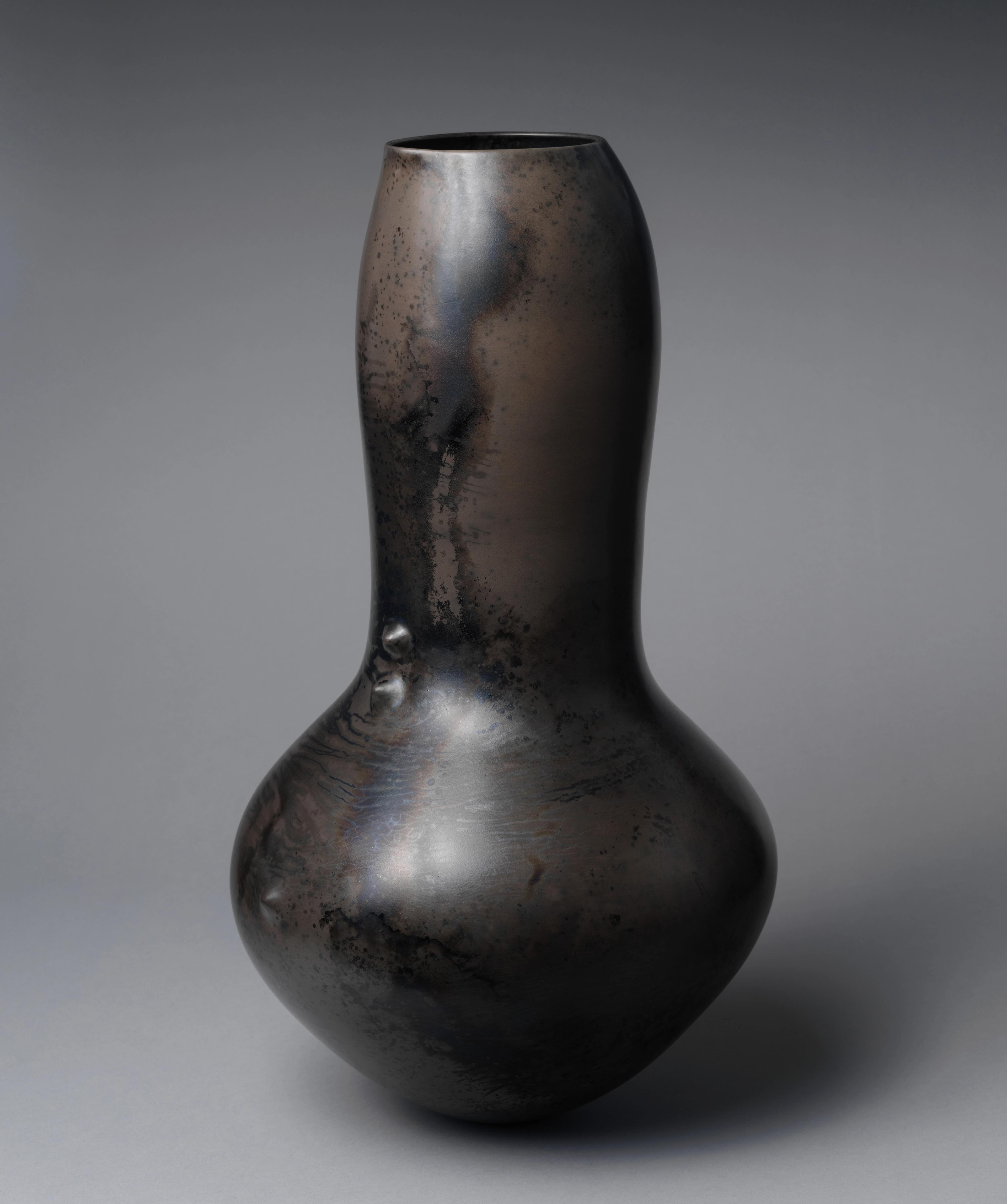 Black ceramic vessel with a rounded body and long, narrow neck, featuring a shiny, burnished surface and two small raised protrusions at the base of the neck.