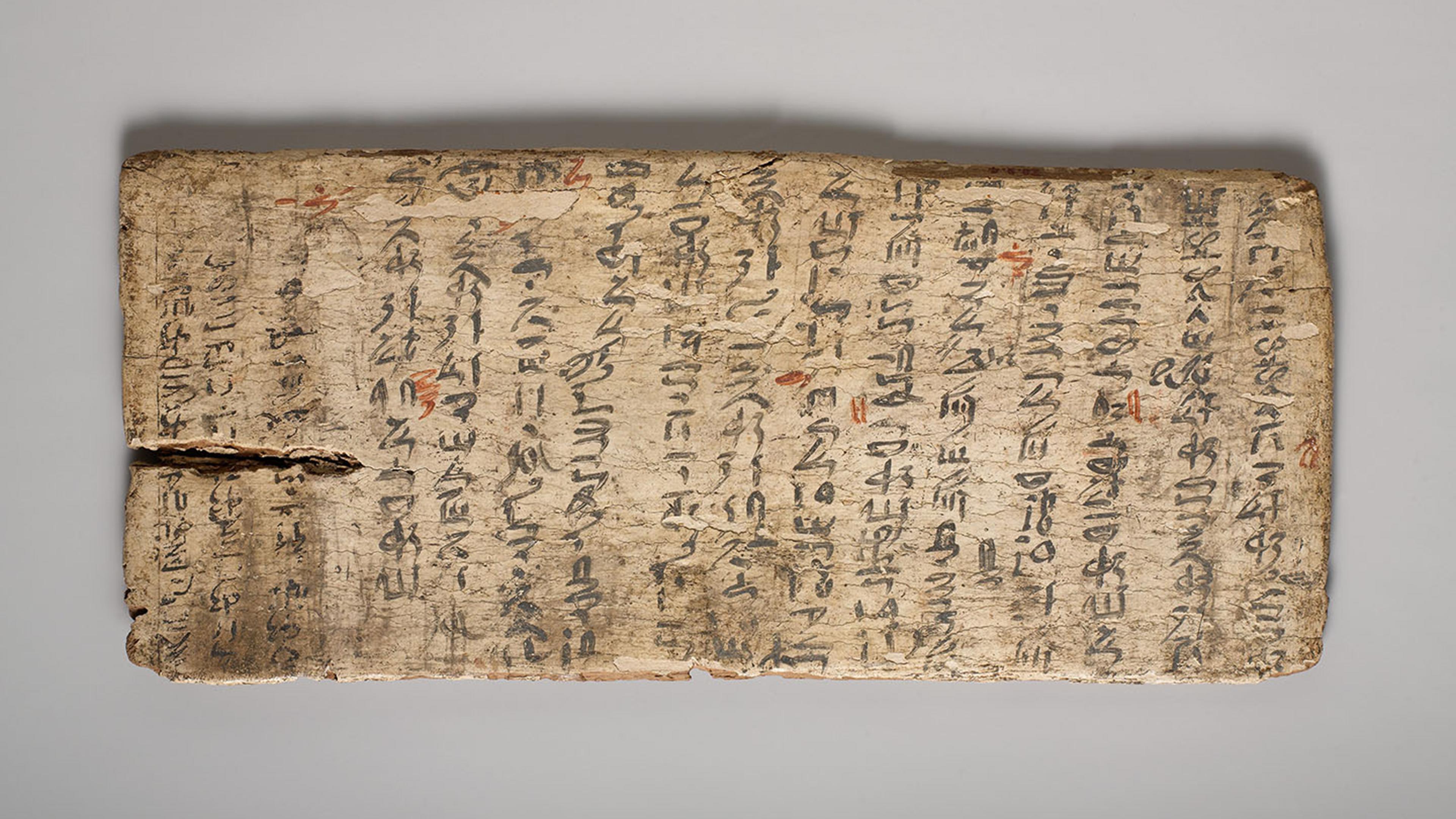 A long rectangular tablet painted mostly with black and some red calligraphic characters in consecutive vertical columns spanning the full width of the tablet