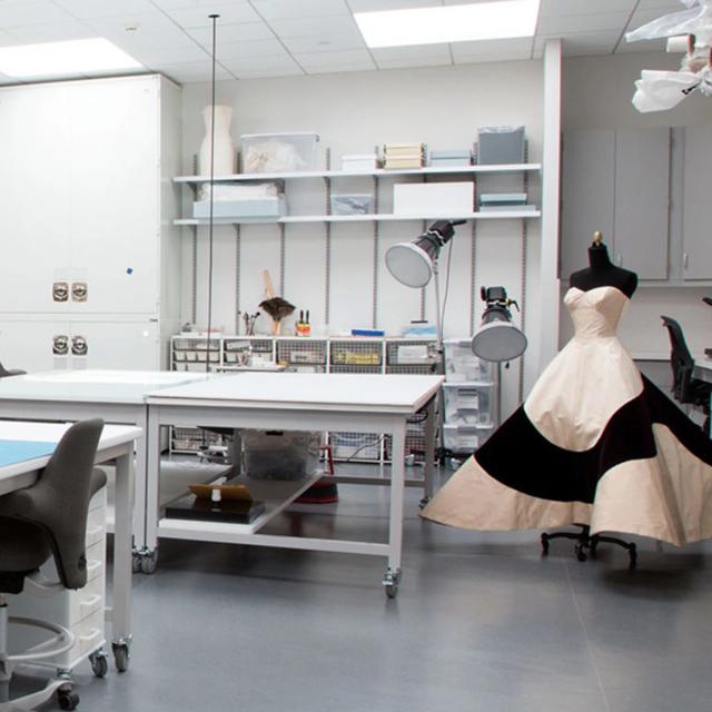 View of the Costume Institute Conservation lab, showing various examination tables, shelves of instruments, and a Charles James couture ballgown in the corner