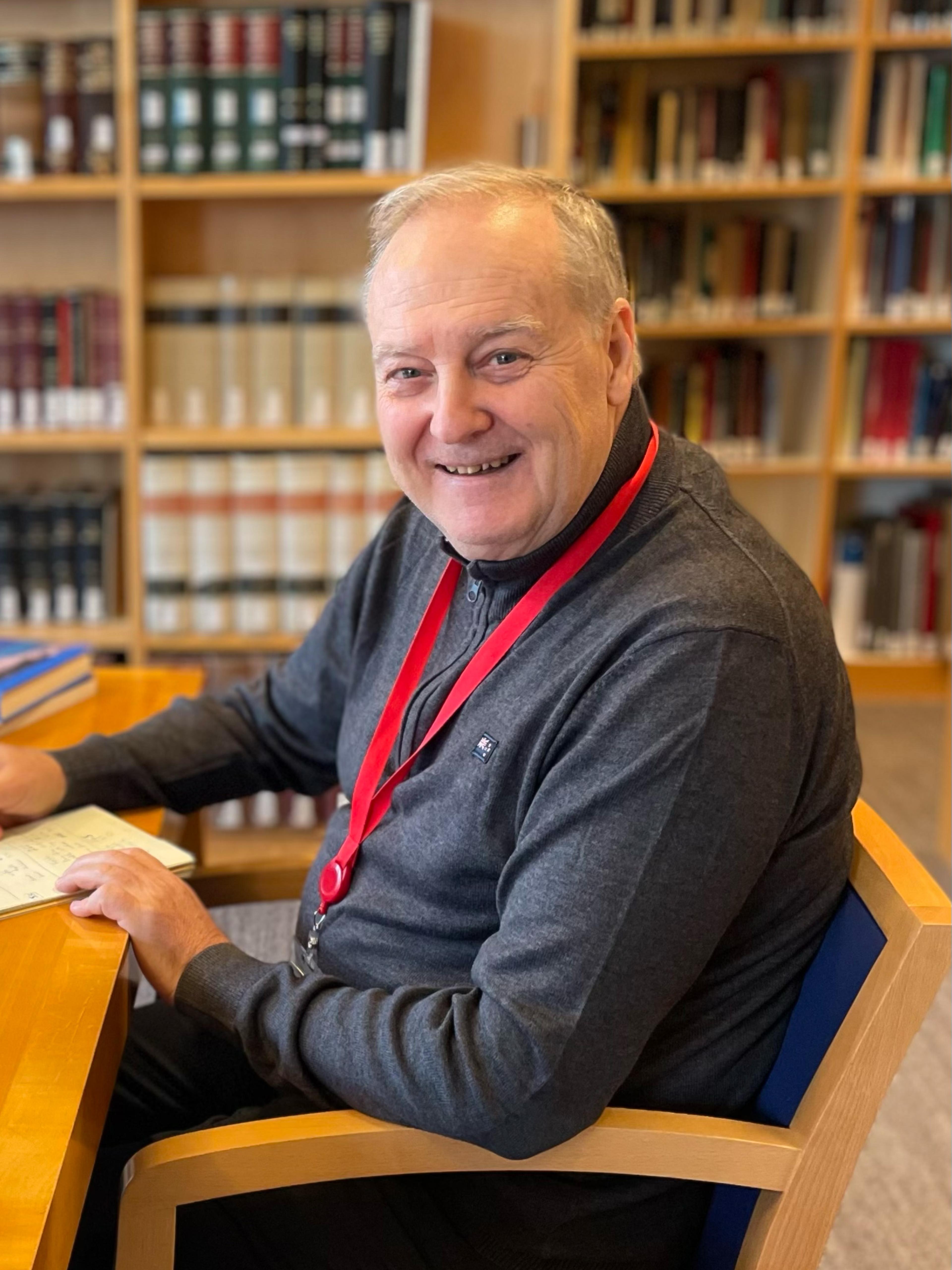 White male sits in desk chair with a smile on his face.