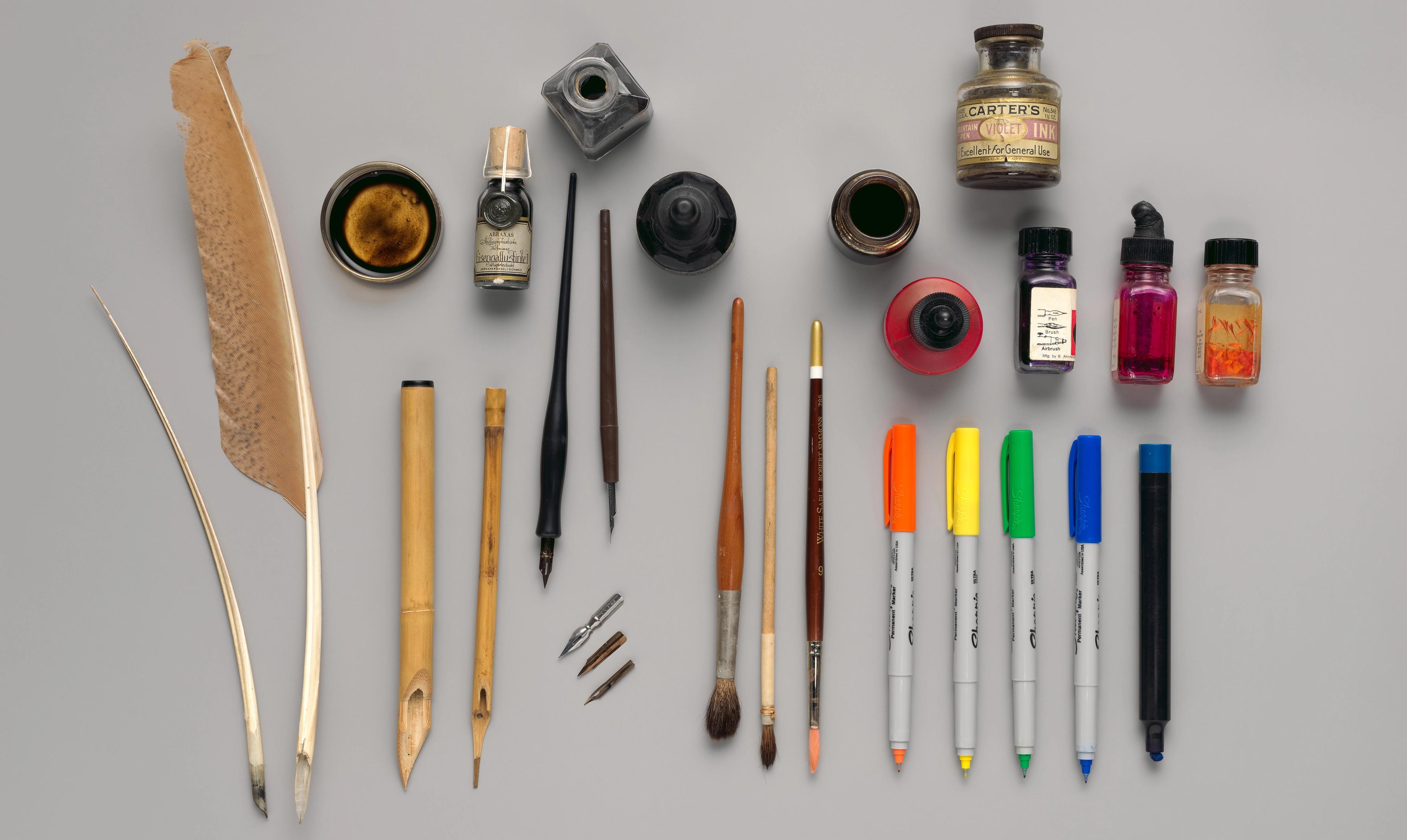 A neat arrangement of inks, pens, and feather quills placed on a grey tabletop.