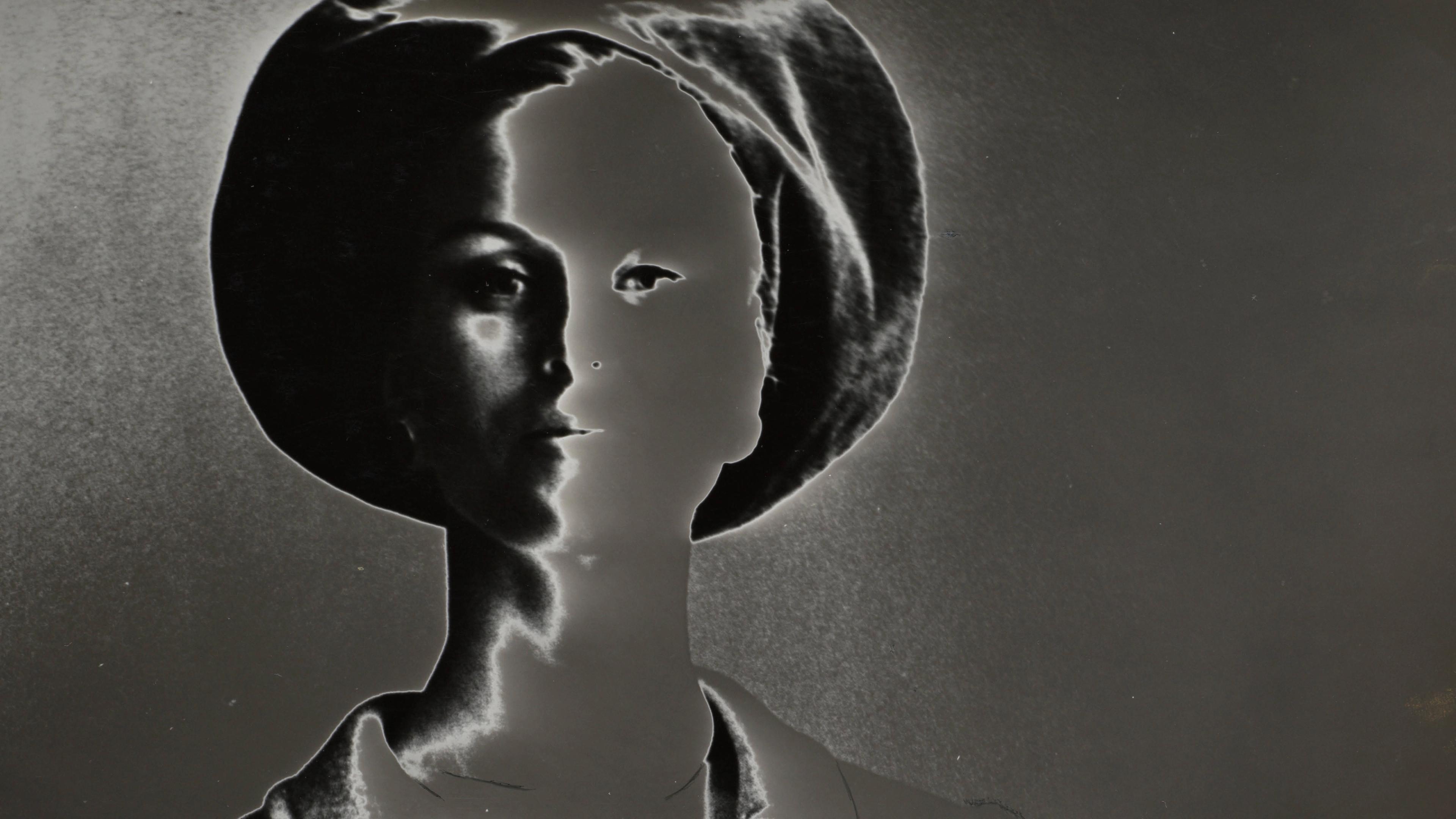 A stylized black-and-white image of a person wearing a hat and jacket, with high contrast and negative effect