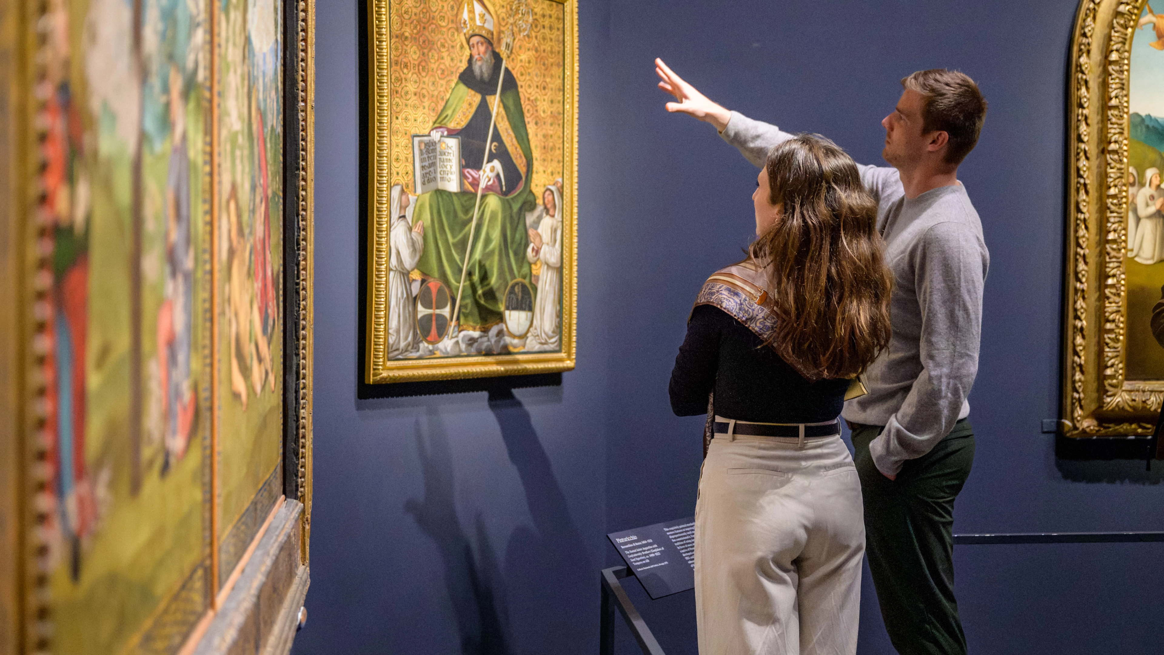 An installation image of visitors pointing at art in the exhibition, Raphael: Sublime Poetry