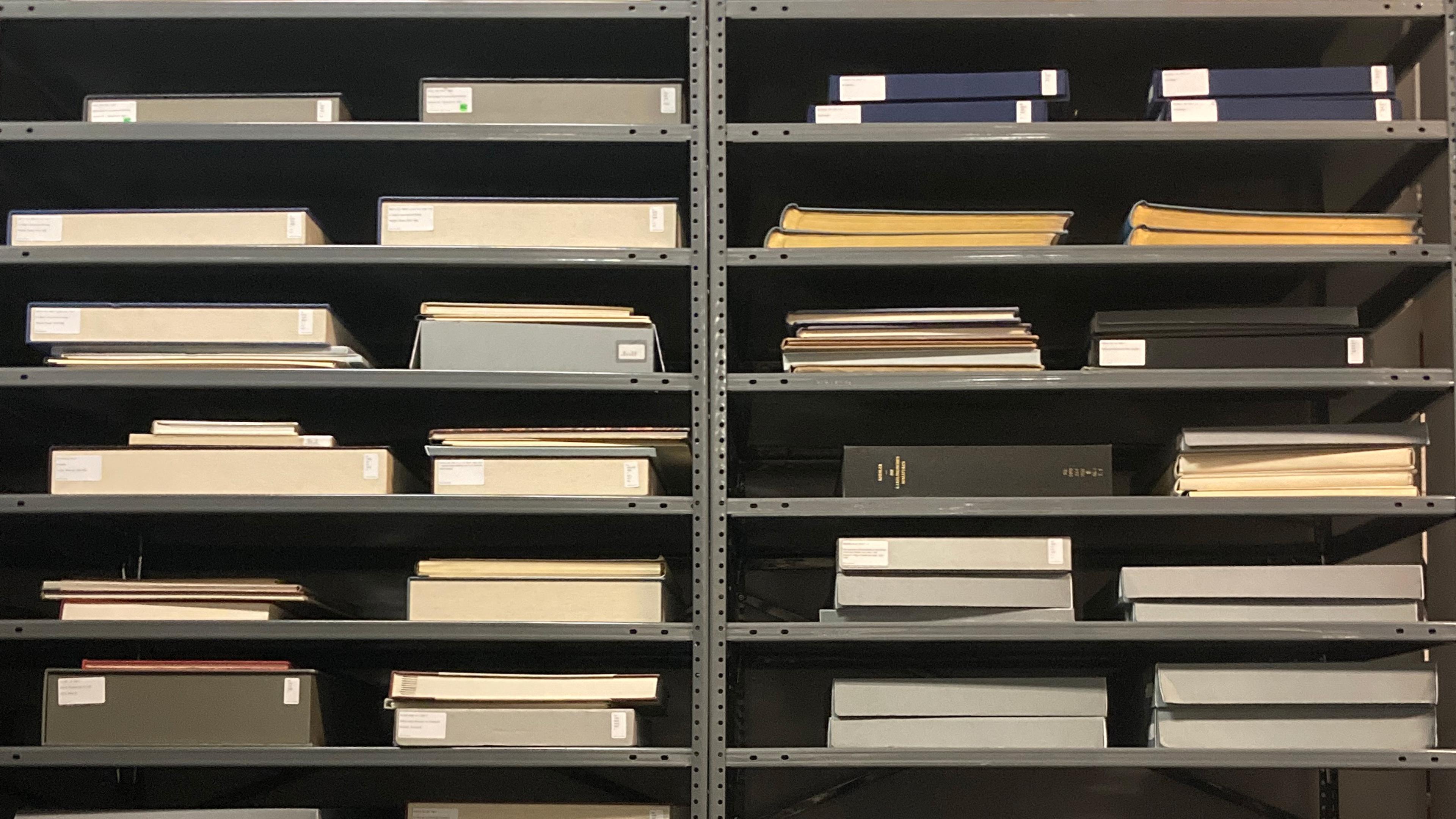 Photograph of folios laying flat on gray, metal shelves