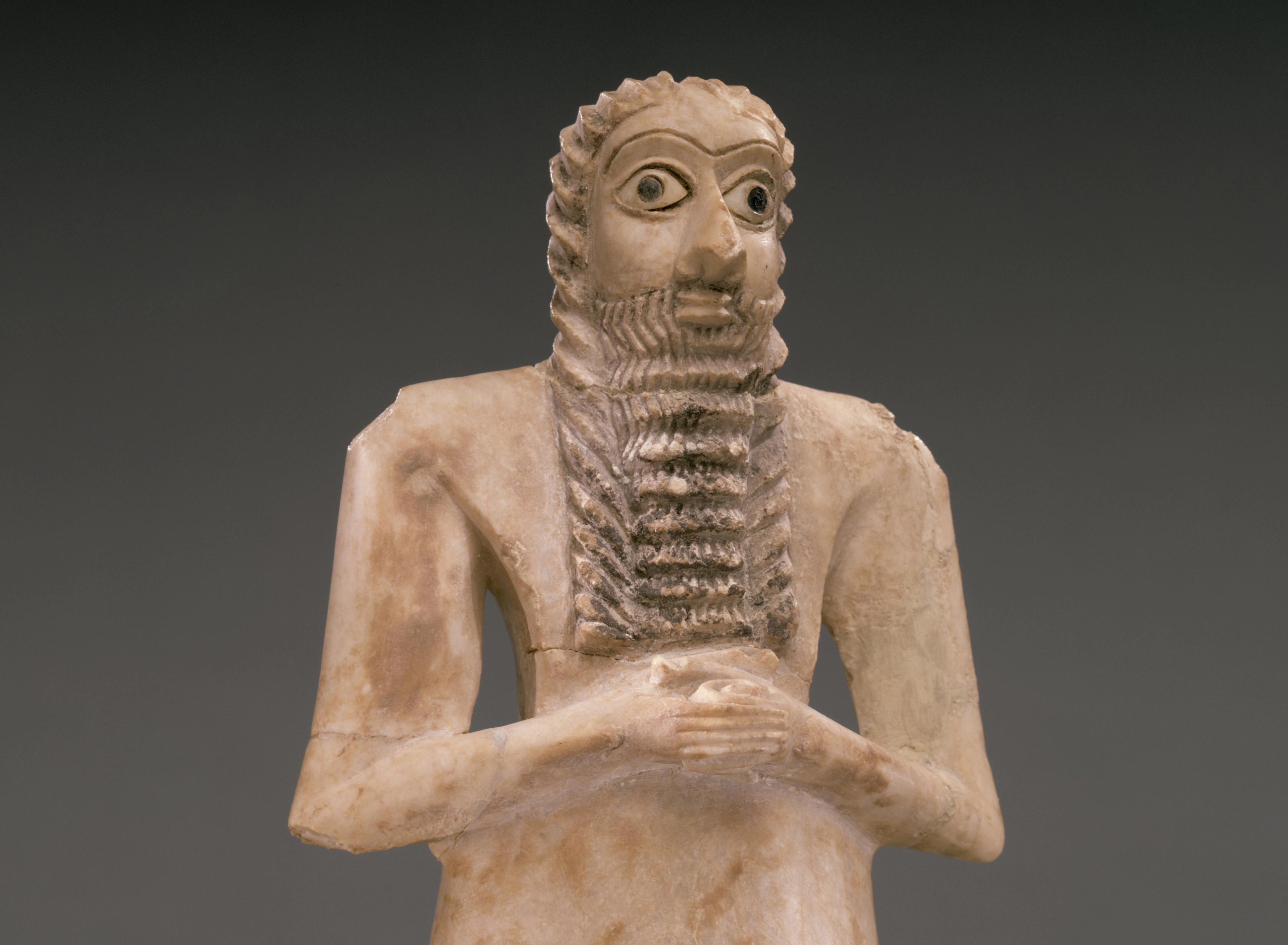 White stone figure with wide eyes and a long, ridged beard, clasping his hands across his chest.