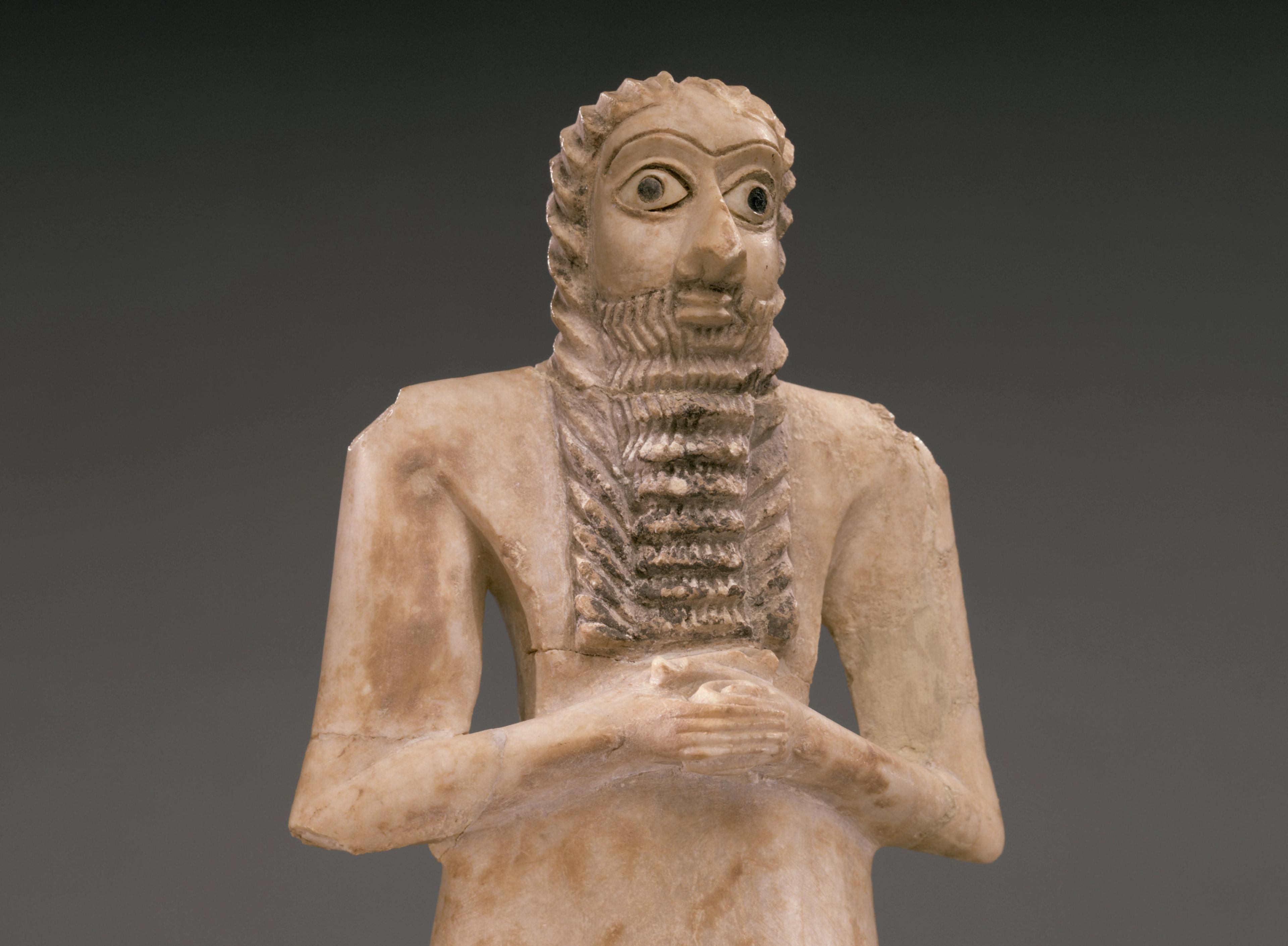 White stone figure with wide eyes and a long, ridged beard, clasping his hands across his chest.