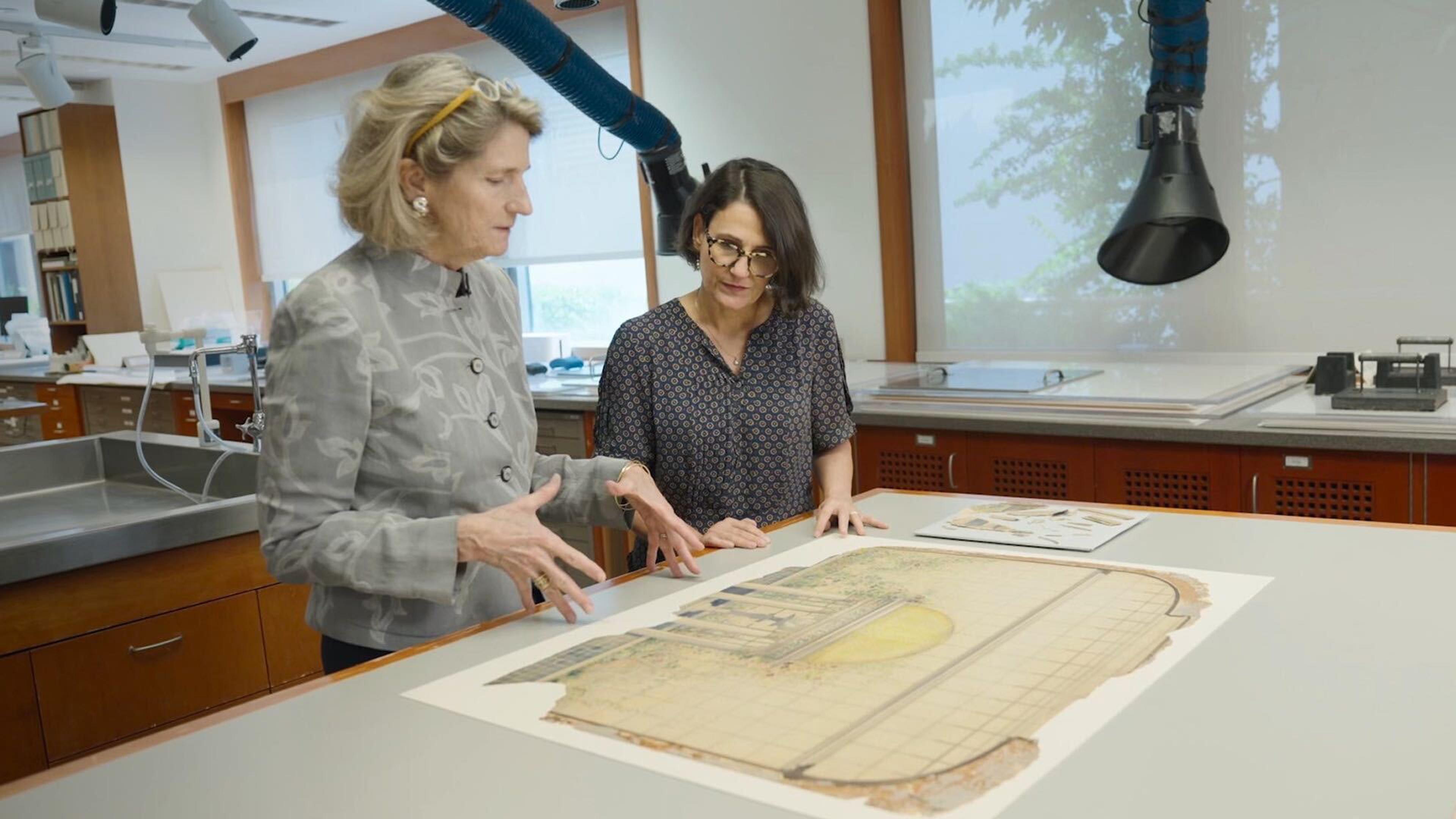 Two people examine a large, damaged drawing on a worktable in a conservation studio