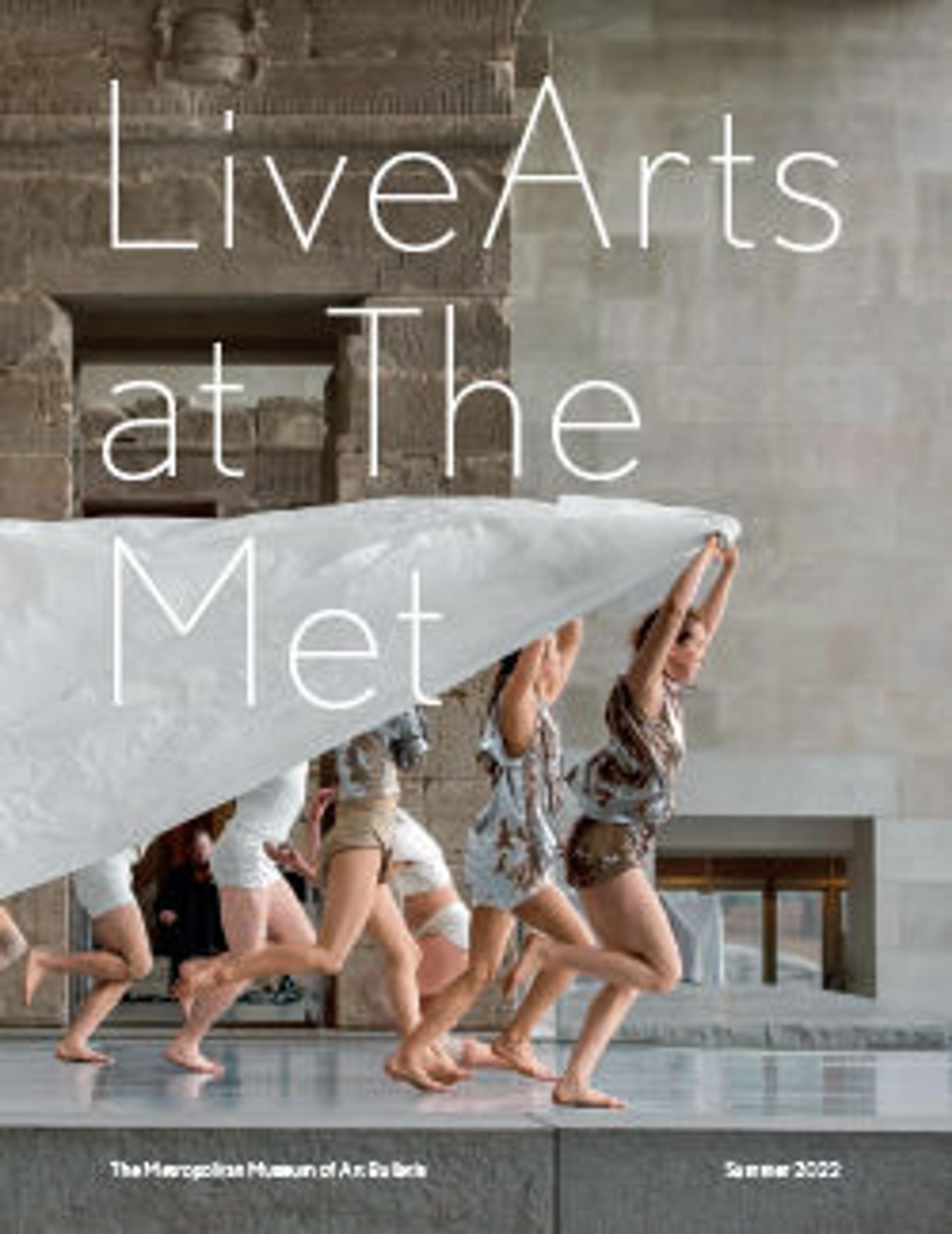 running dancers pulling a cape of white fabric past a large stone entryway on display at a museum