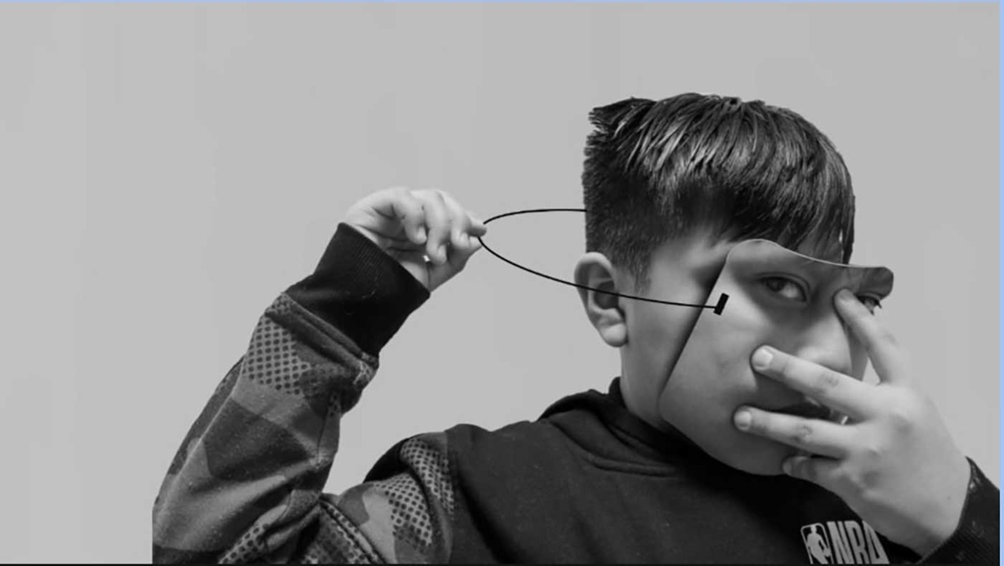 Picture of a young boy taking off a realistic-looking mask of a face.