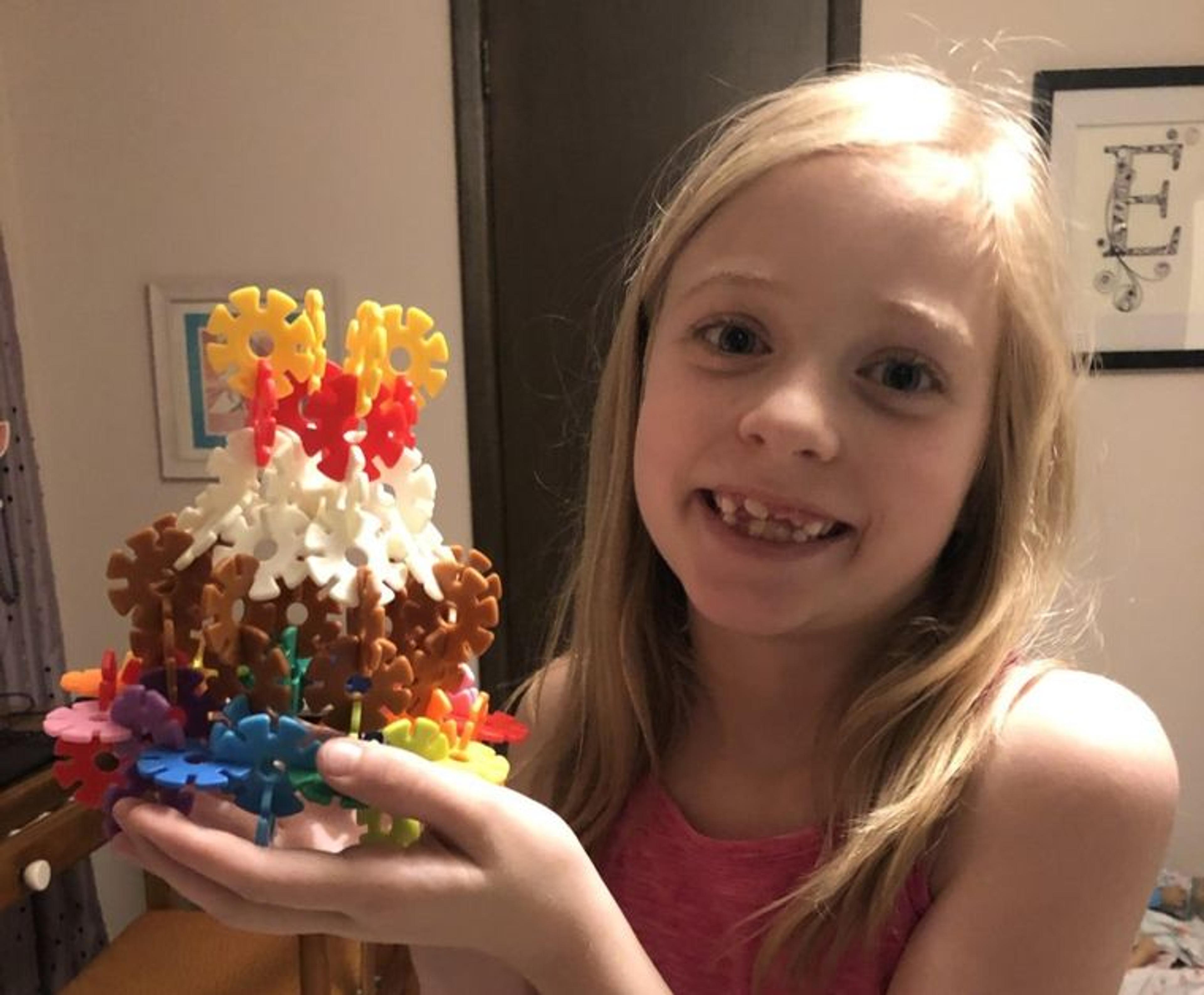 A blonde elementary school student holds a colorful cake made from plastic parts