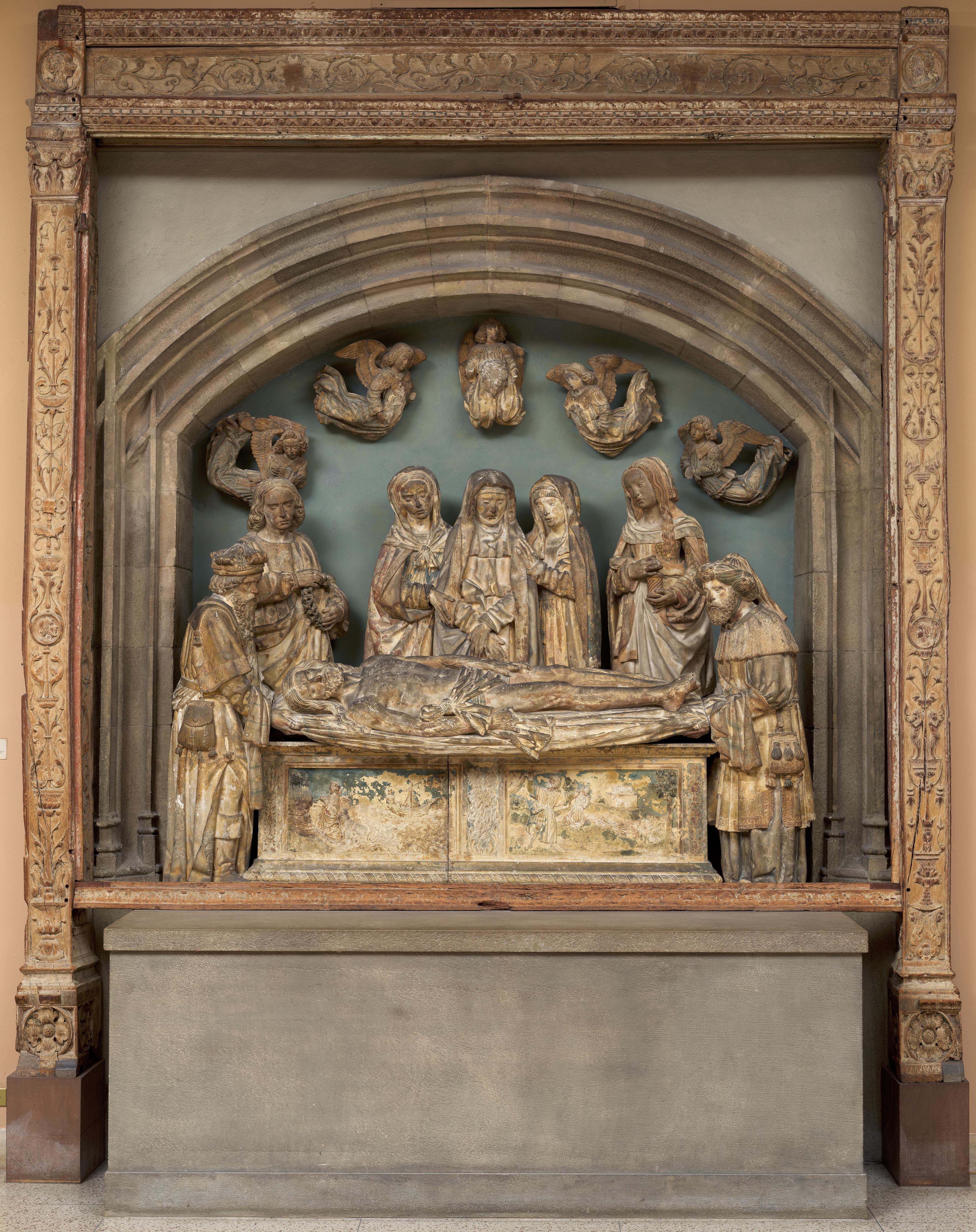 Ornate wood frame with scroll motifs surrounding a medieval sculpture.
