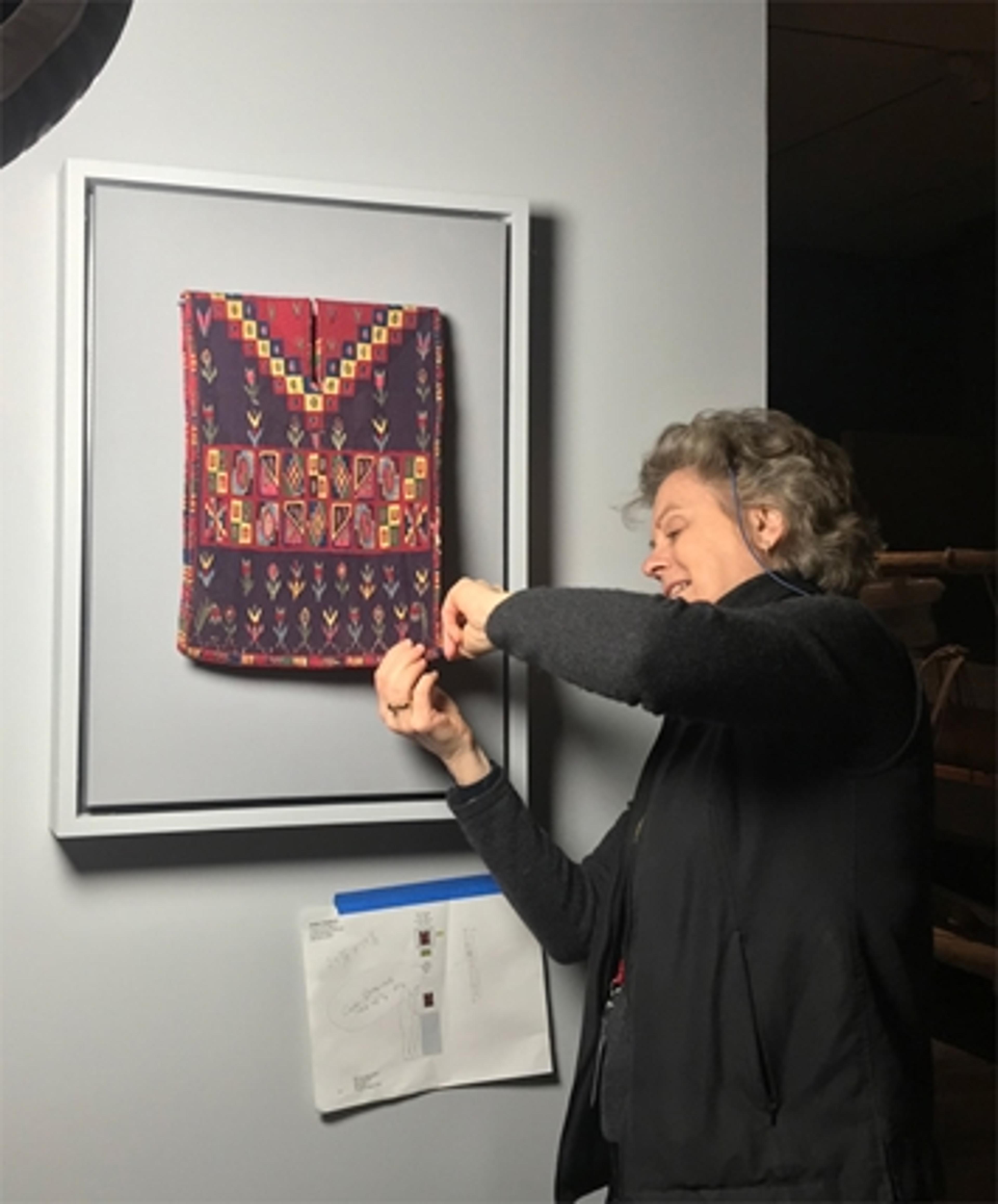 A Met conservator ensures that a wall hanging is properly secured in an exhibition gallery