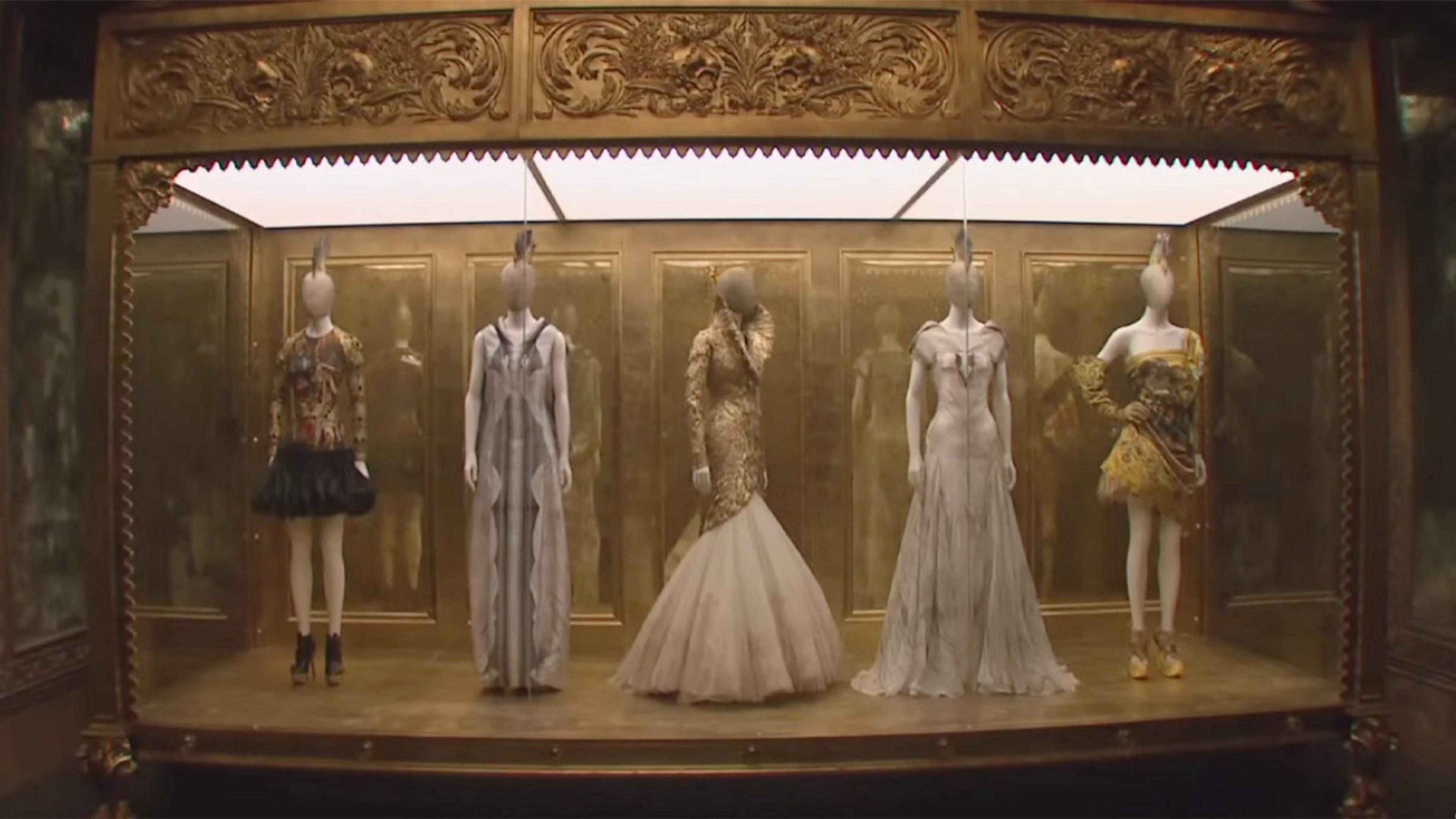 Ornate, golden, carnival-esque display case with five mannequins.