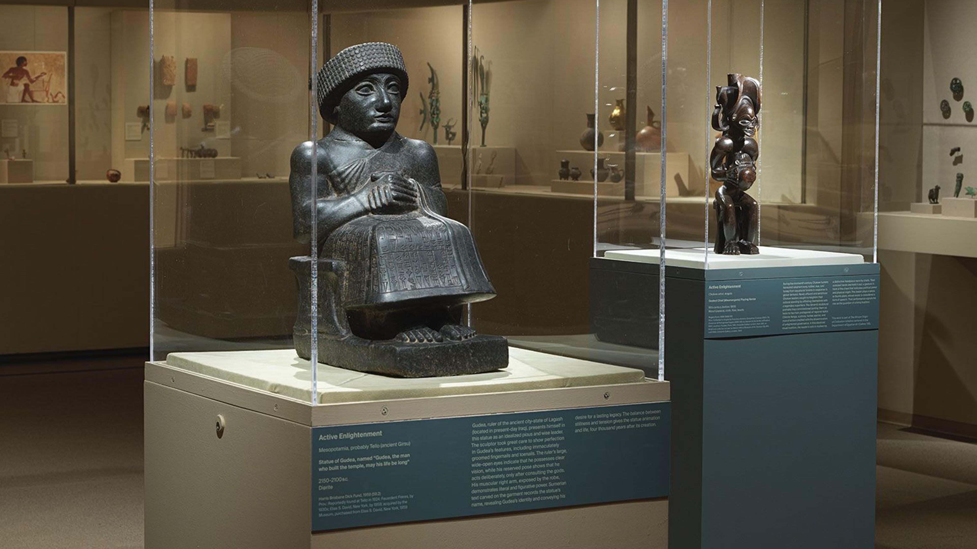 Two sculptures displayed in glass cases at a museum, one depicting a seated figure and the other a dynamic, abstract form.