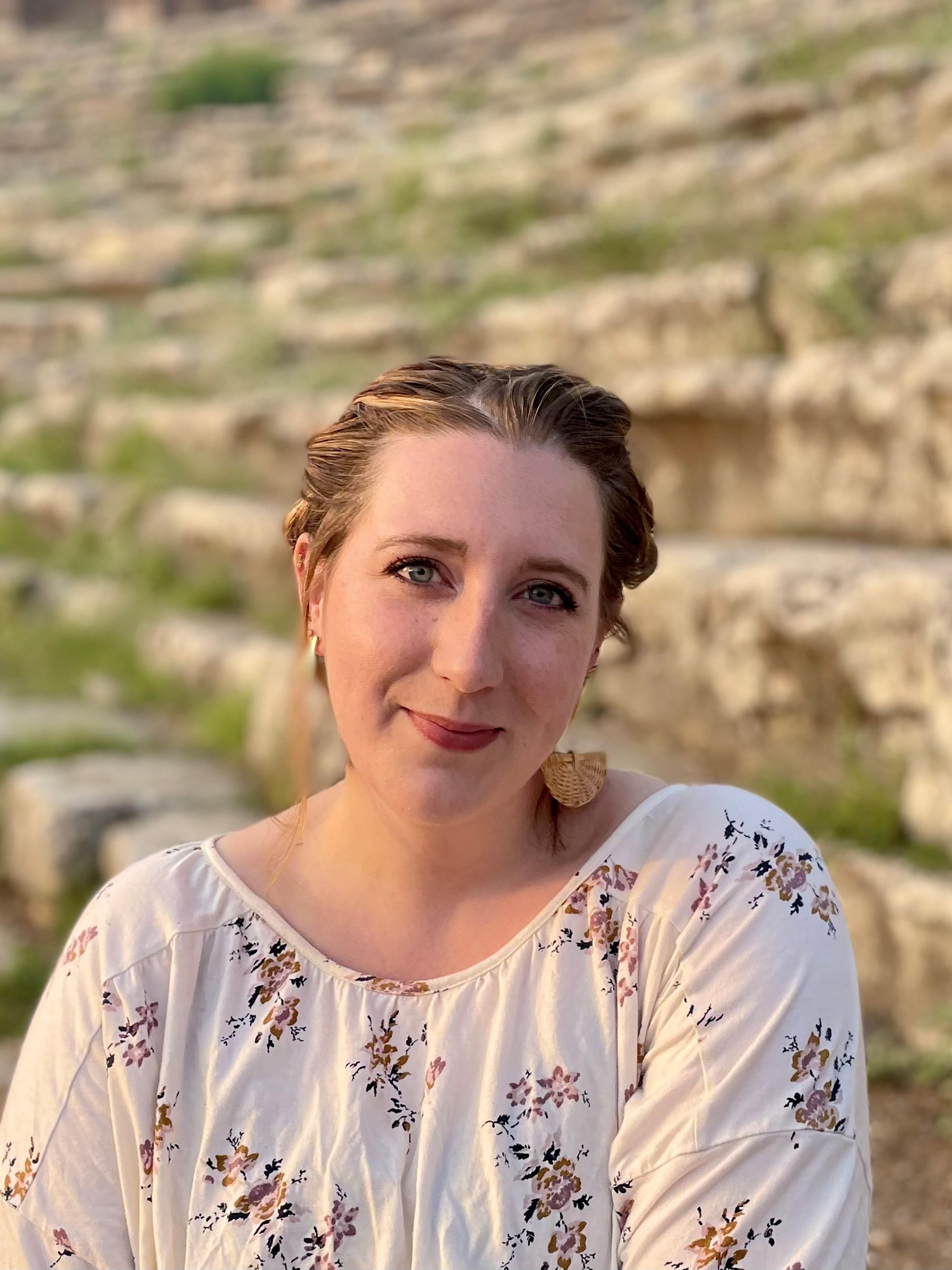 A woman wearing a floral blouse poses in front of an ancient stone wall