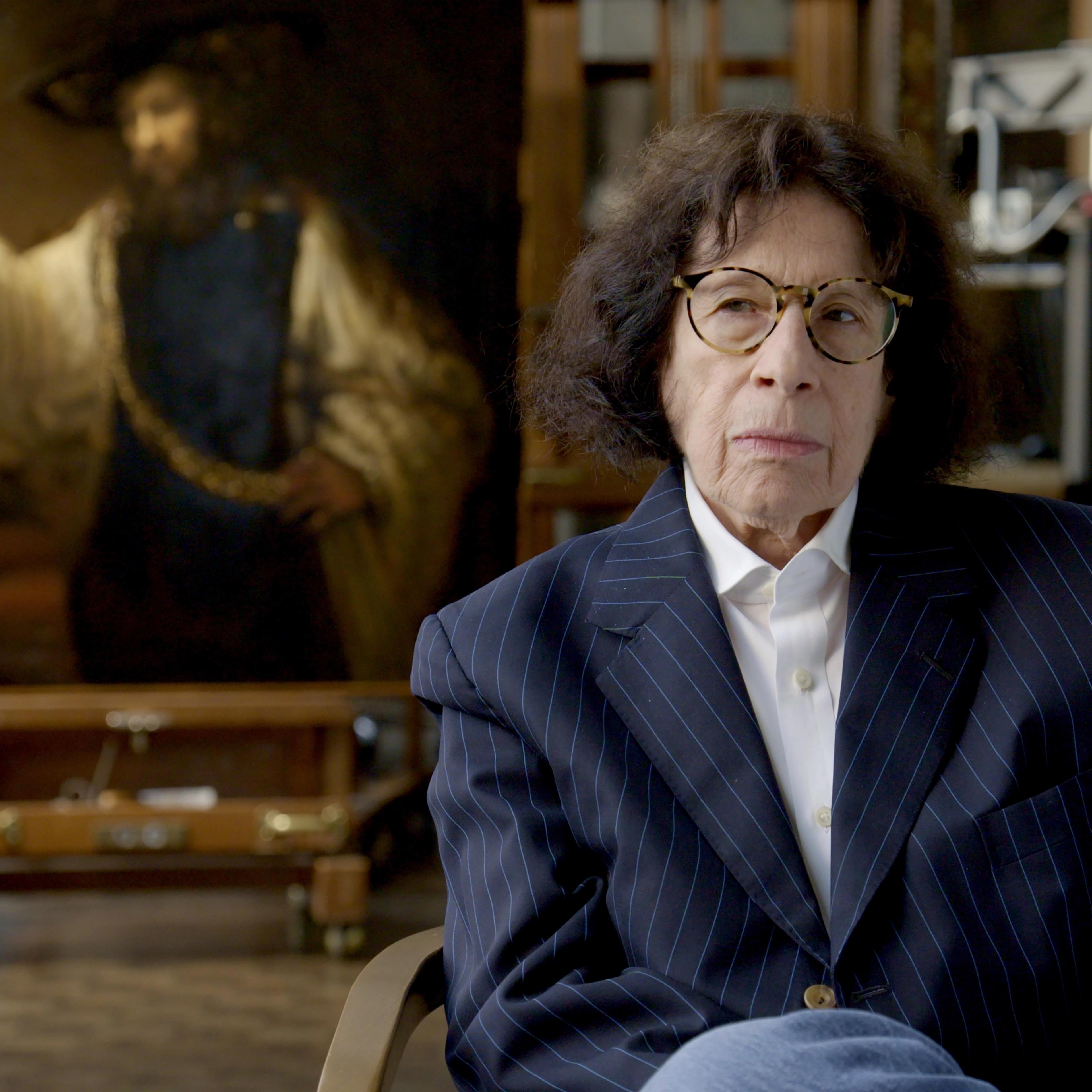 Writer Fran Lebowitz sits in The Met’s Paintings Conservation Lab in front of Rembrandt’s Aristotle with a Bust of Homer painting.