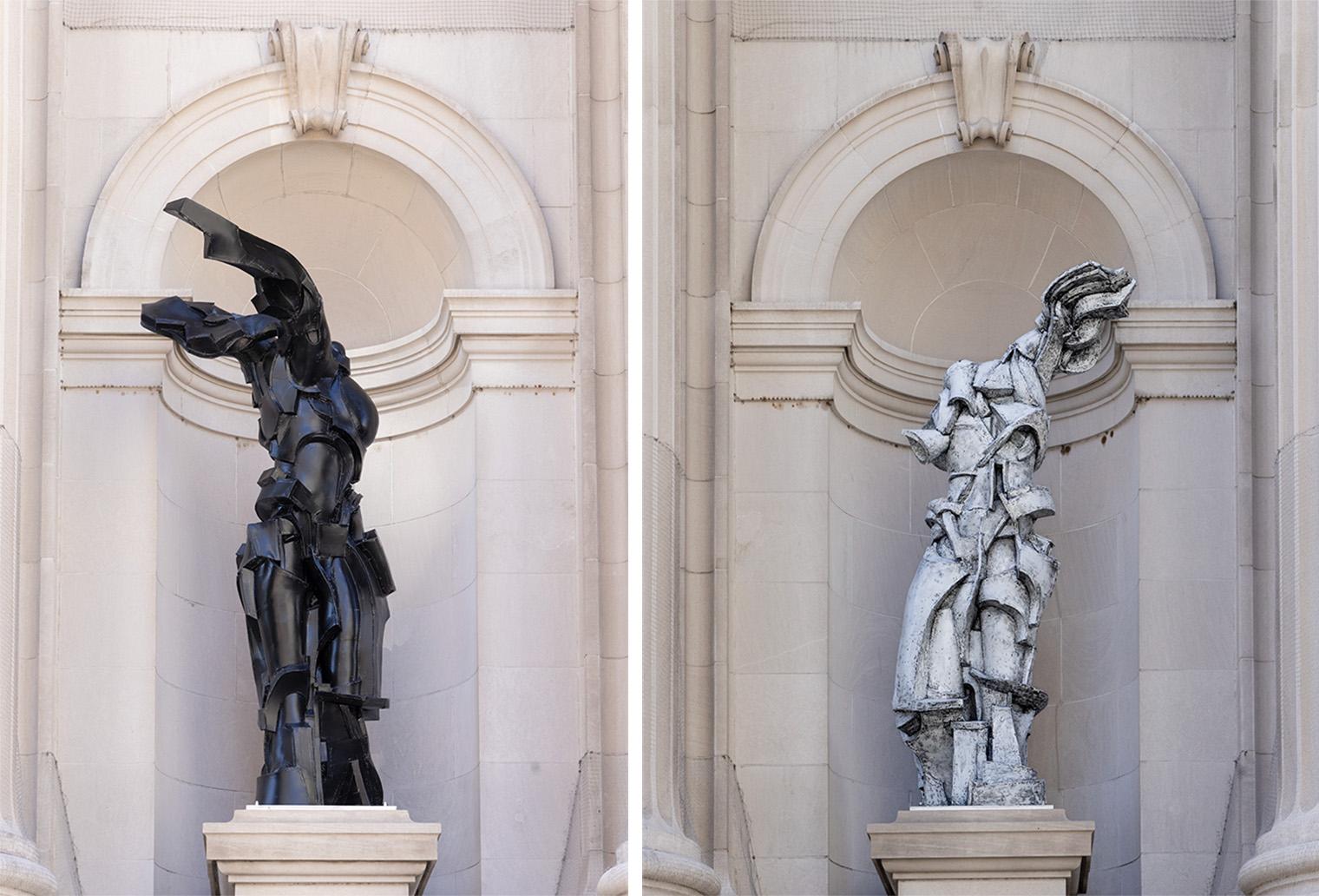Two statuesque figures on the left a black, and on the white rustic white, standing tall outside of building structure.