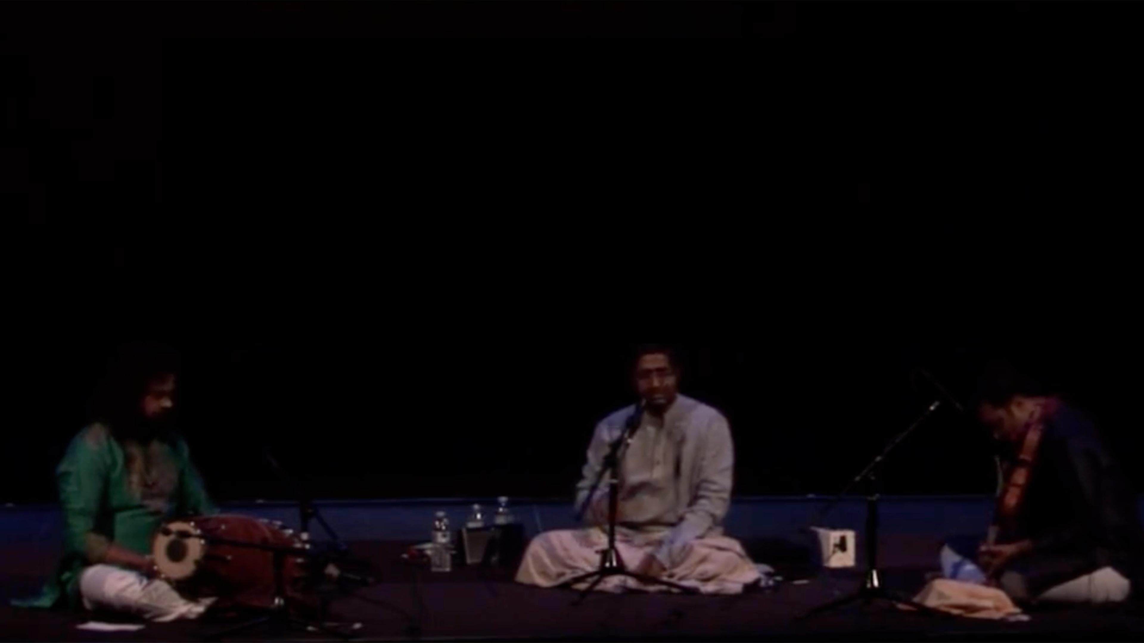 Three musicians seated on a dark stage