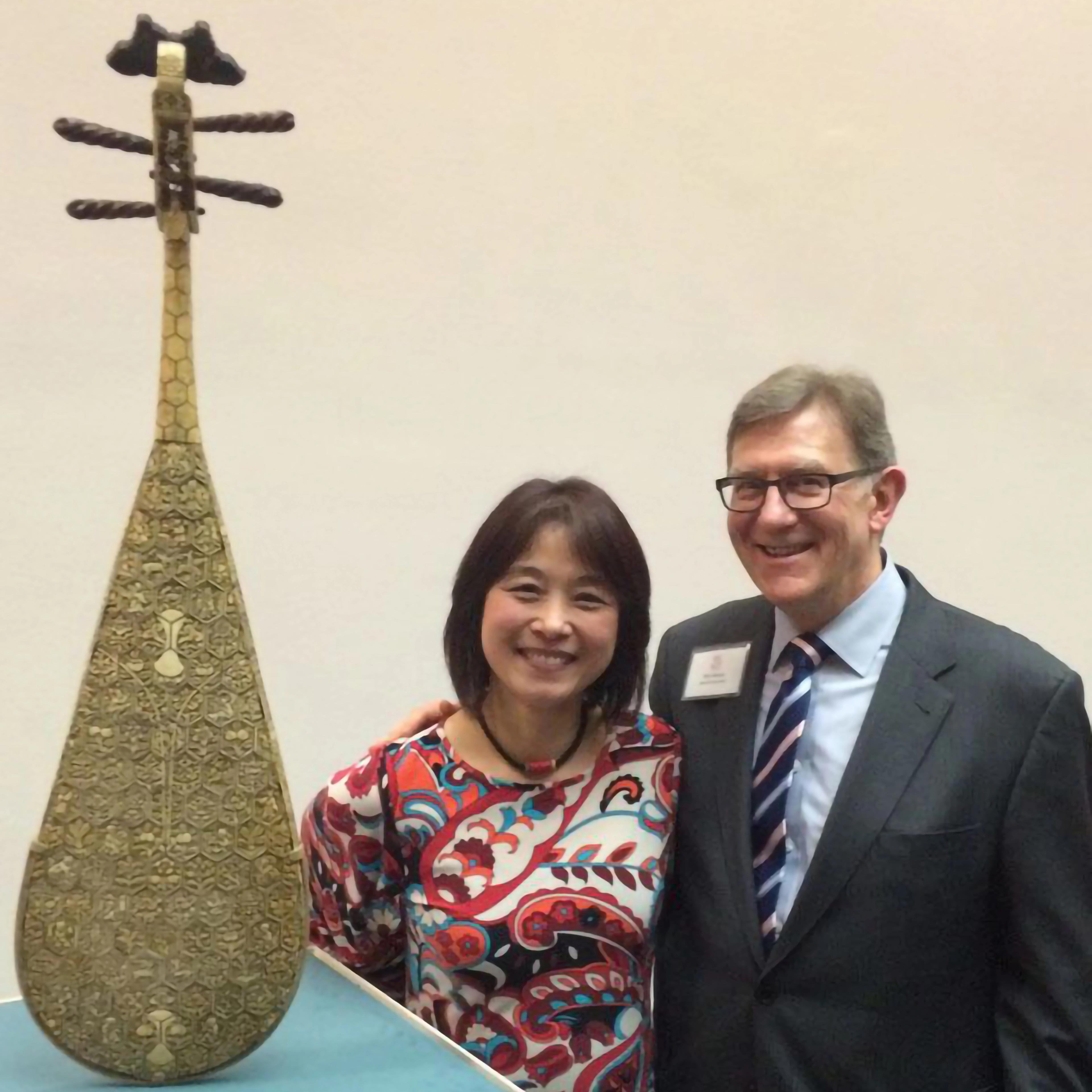 Wu Man and Ken Moore stand smiling next to an ornate pipa elevated on a pedestal.