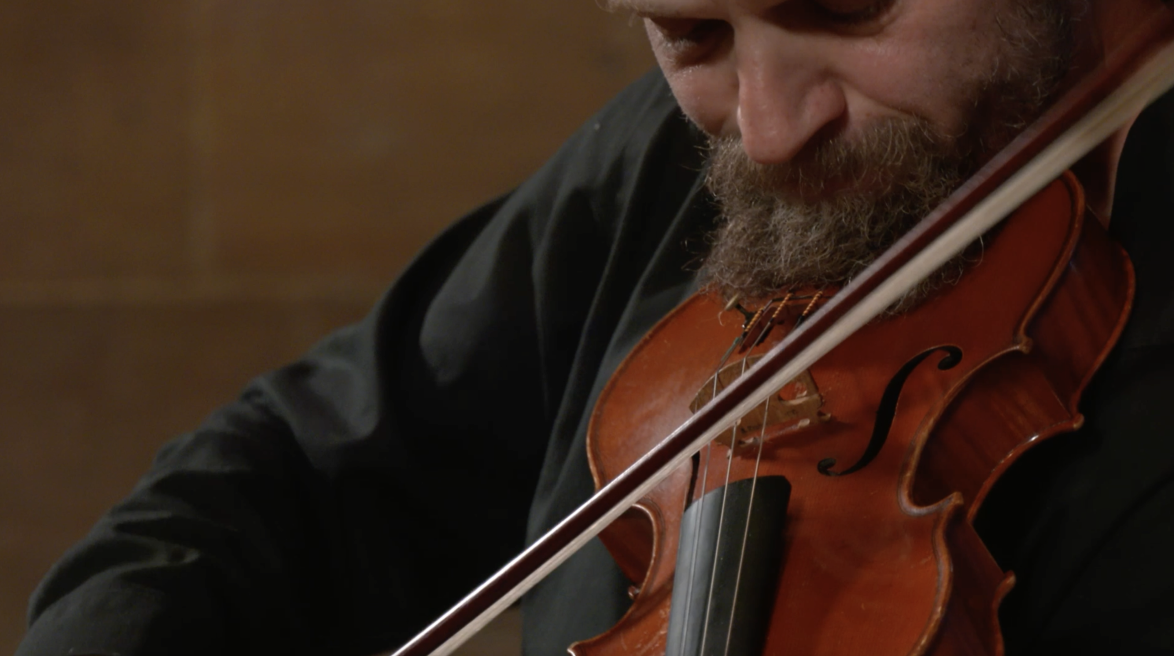 Close up shot of a man in all black playing the violin. 