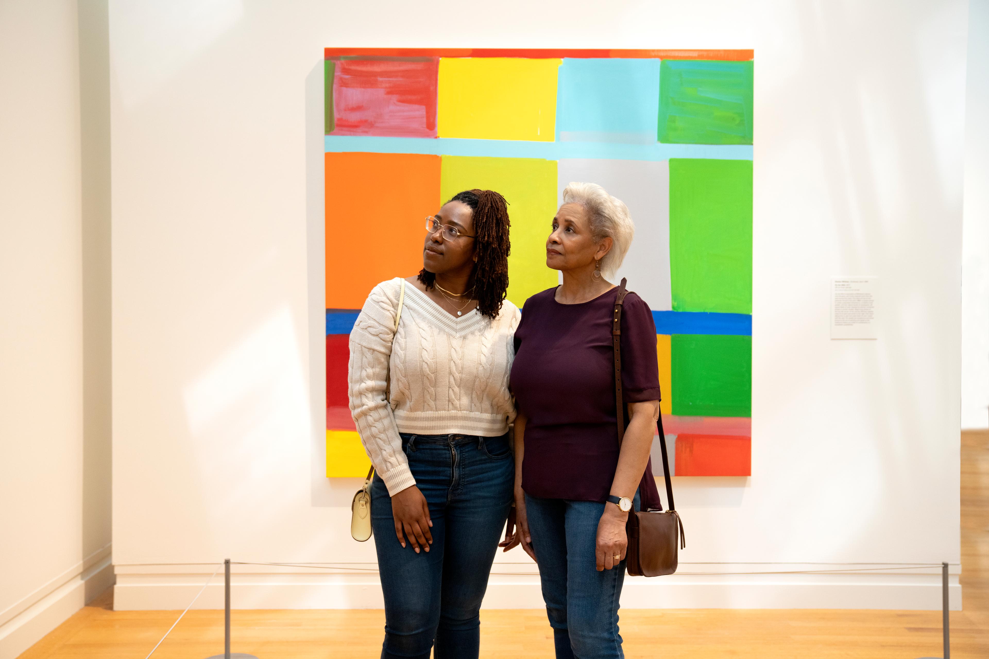 Two Black women, one older and one younger, stand contemplatively in The Met's Modern and Contemporary Wing in front of a bright abstract painting.