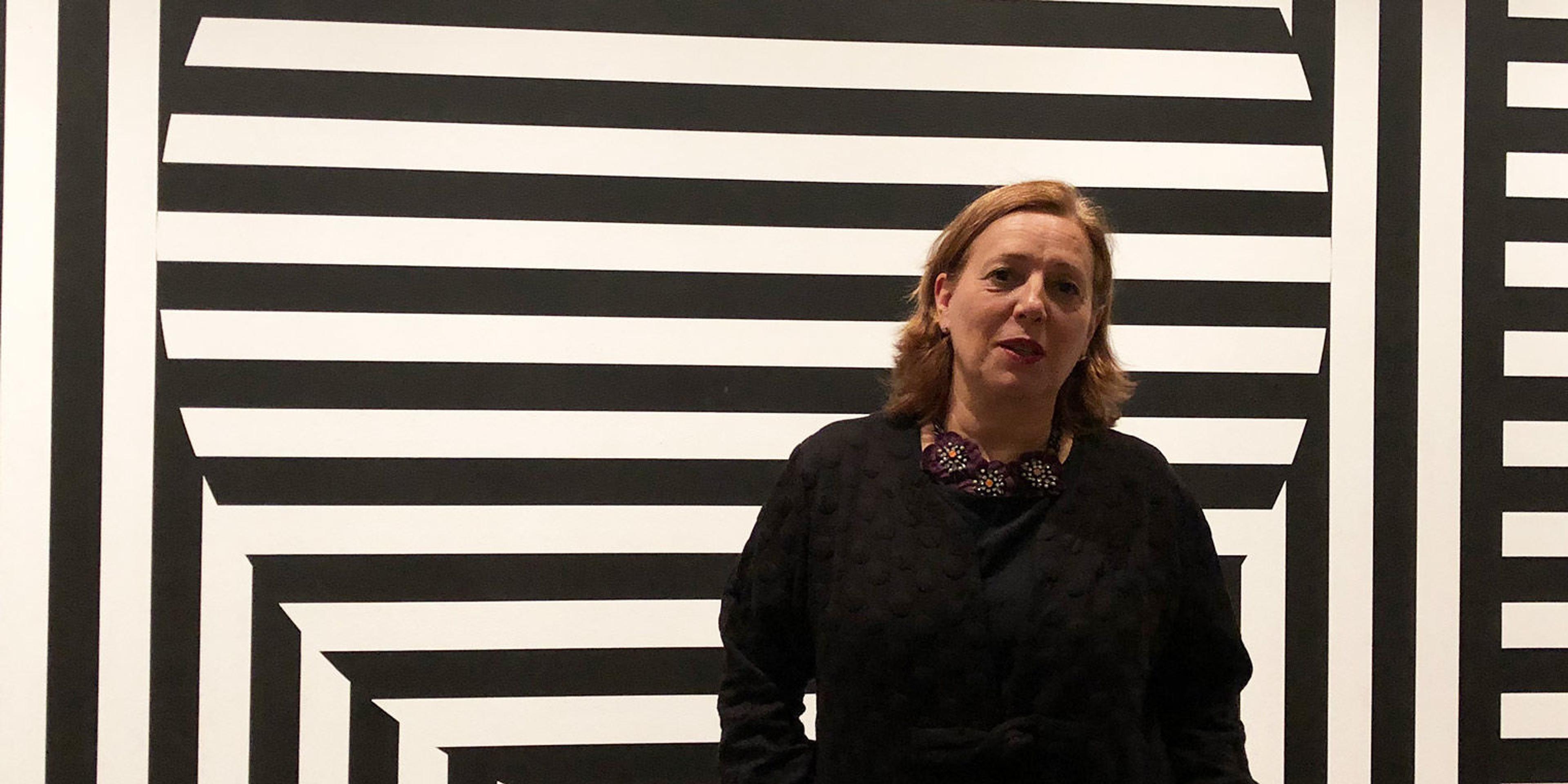 Woman in black standing in front of huge black and white striped wall painting by Sol Lewitt