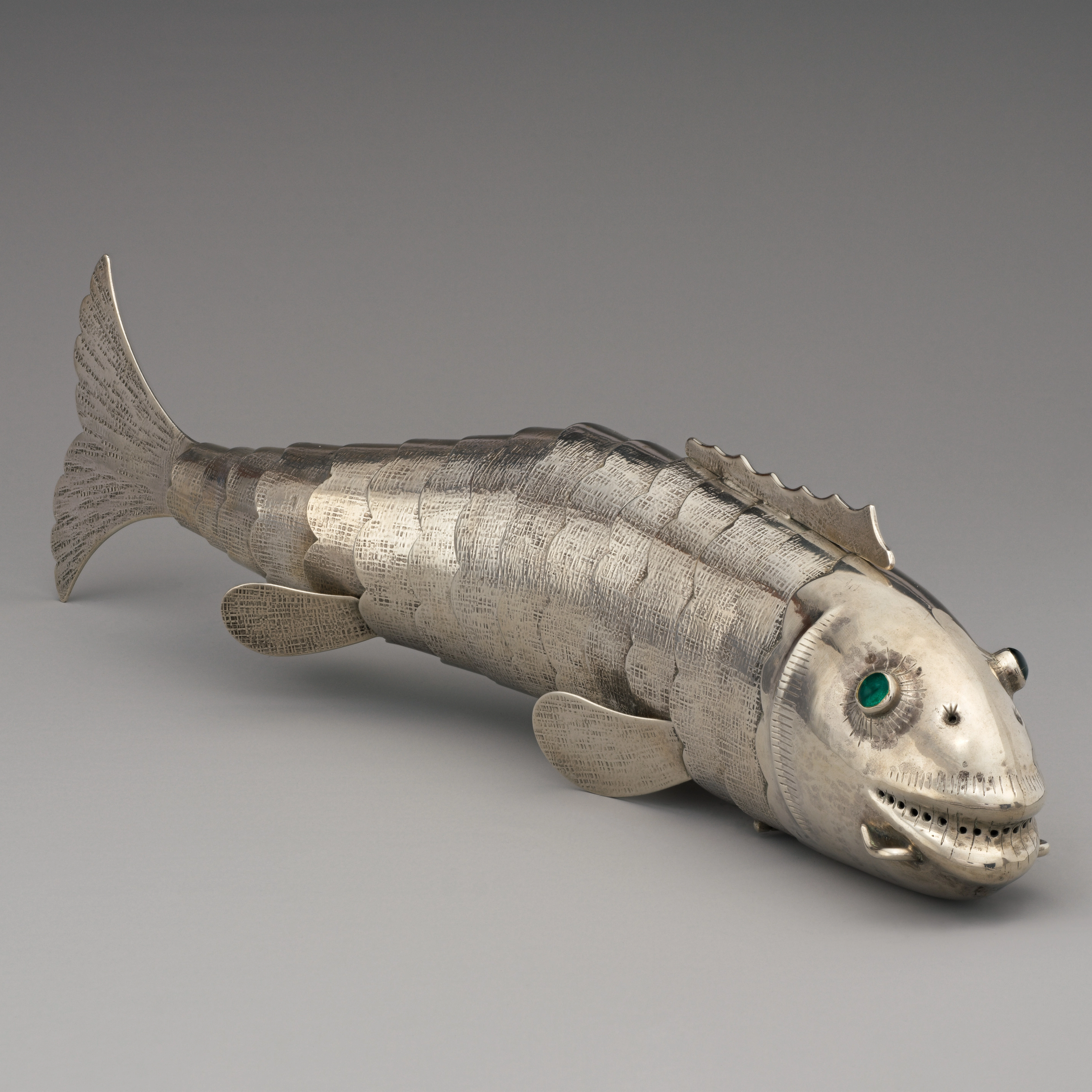 Silver fish sculpture with emerald green eyes, lifelike scales, and visible details.