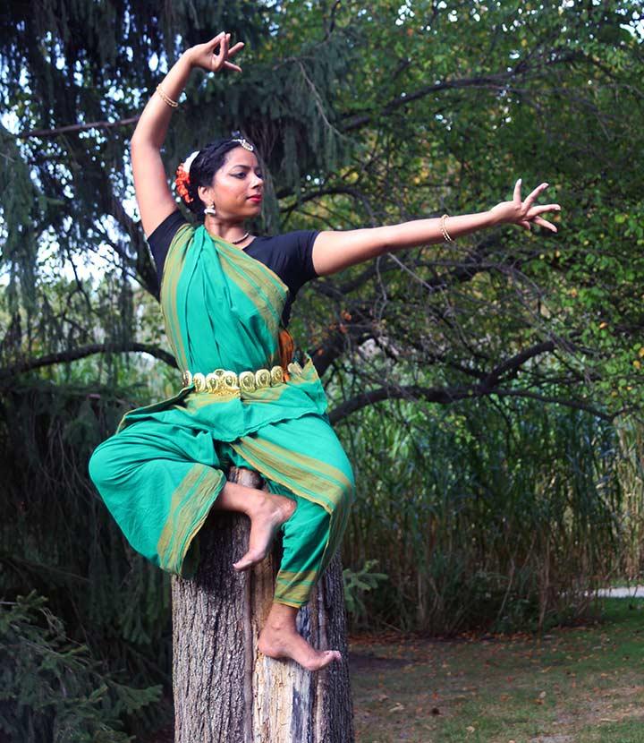 A dancer sitting on a tree stump who looks like she is levitating.