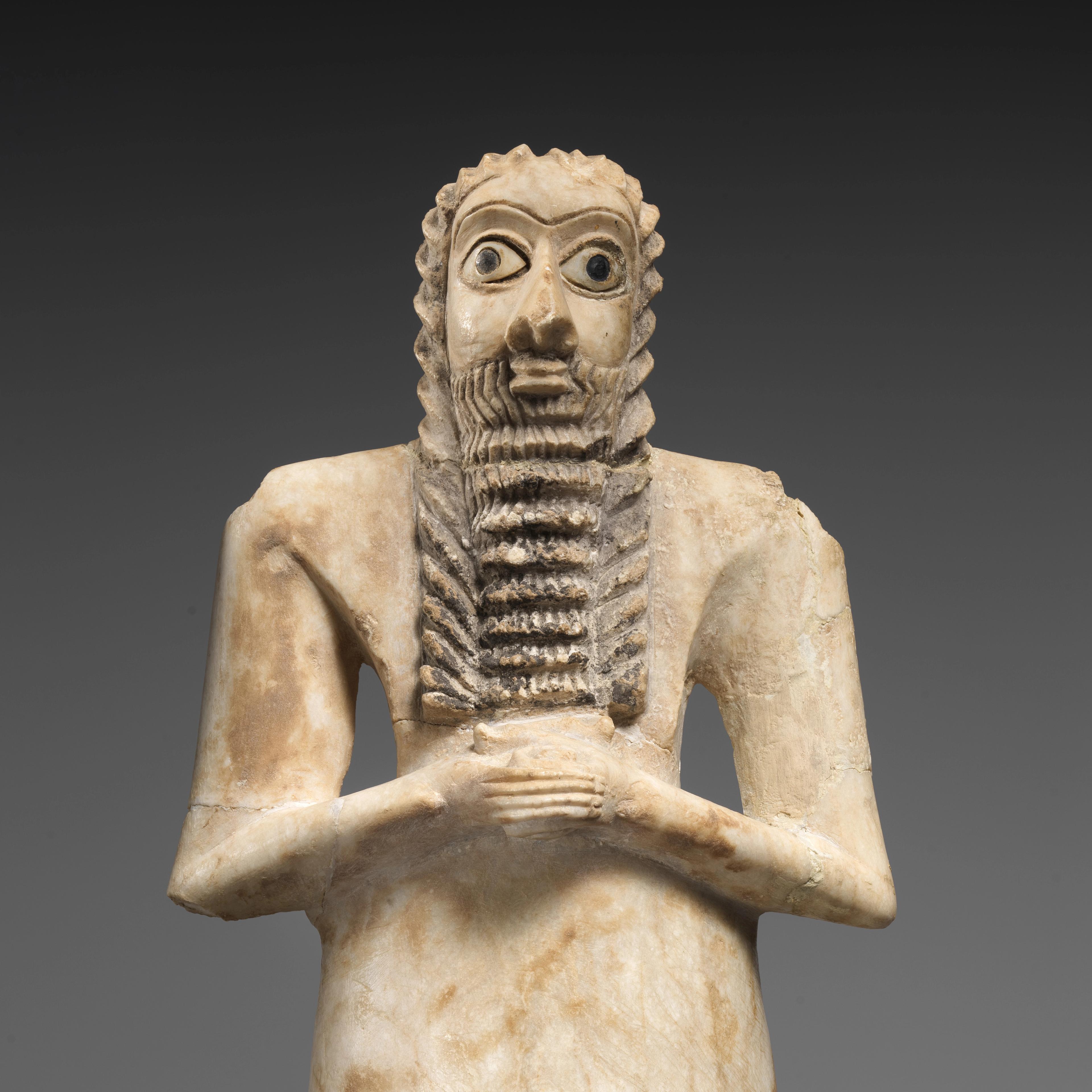 White stone figure with wide eyes and a long, ridged beard, clasping his hands across his chest.