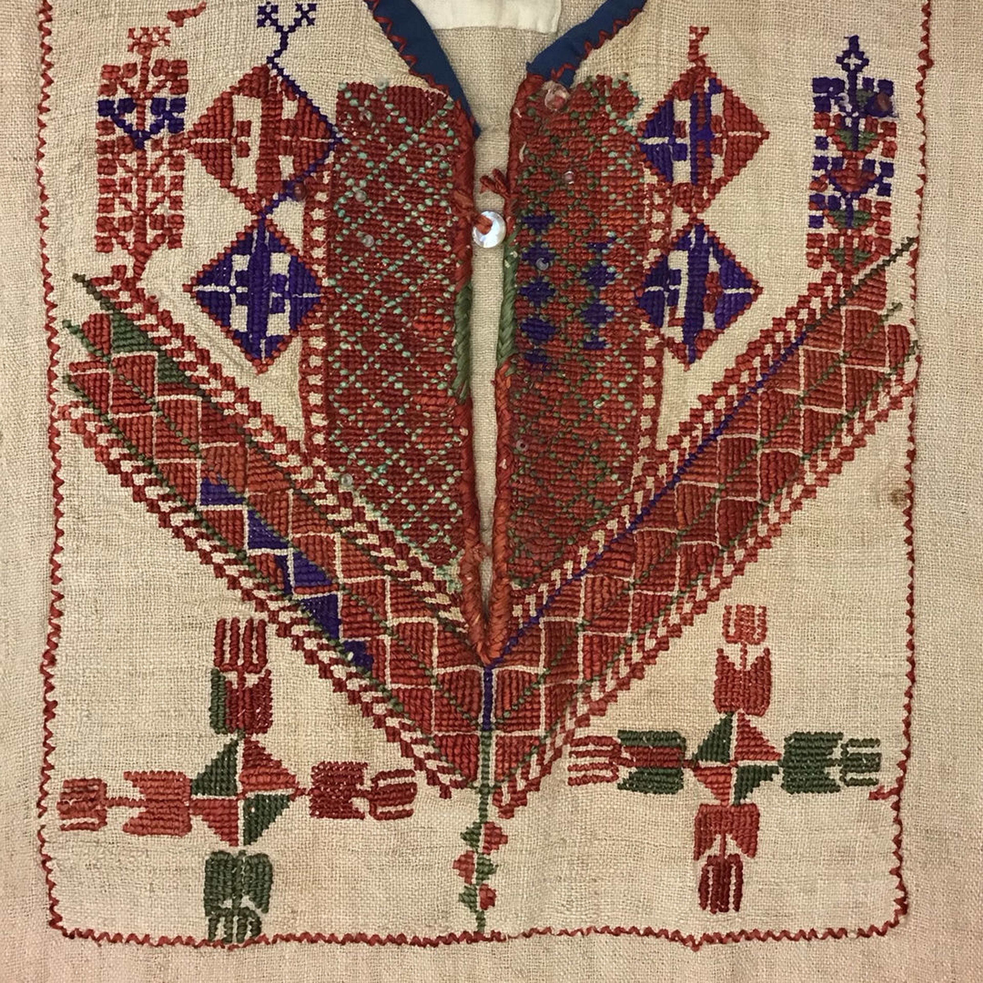 The chest panel of an embroidered thobe. The embroidery accents the beige linen fabric with reds, greens, and blues in symmetrical, geometric patterns.