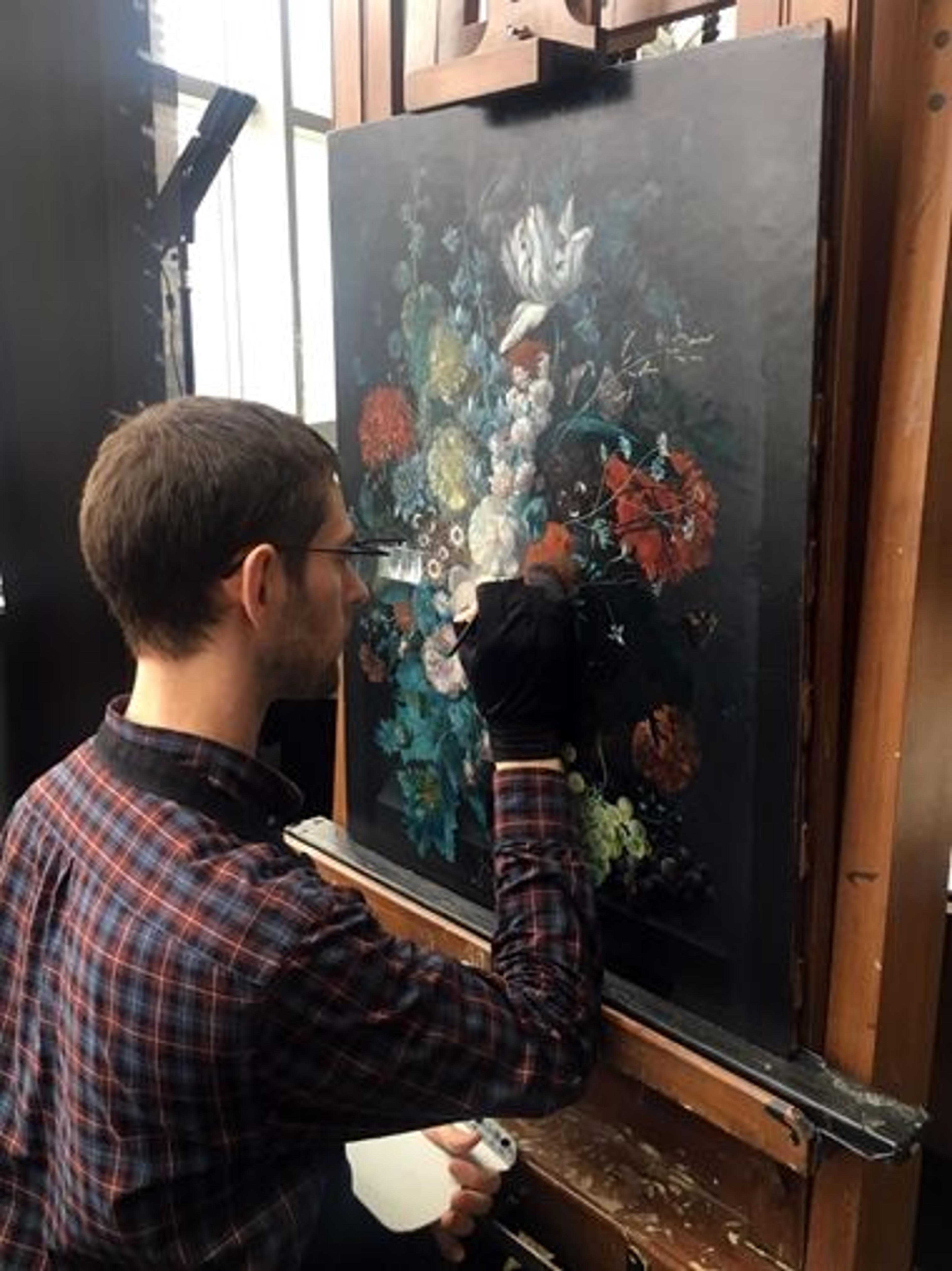 A conservator retouches small damages to a Dutch Golden Age painting of a vase of flowers in a conservation studio