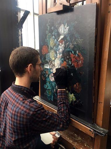 A conservator retouches small damages to a Dutch Golden Age painting of a vase of flowers in a conservation studio
