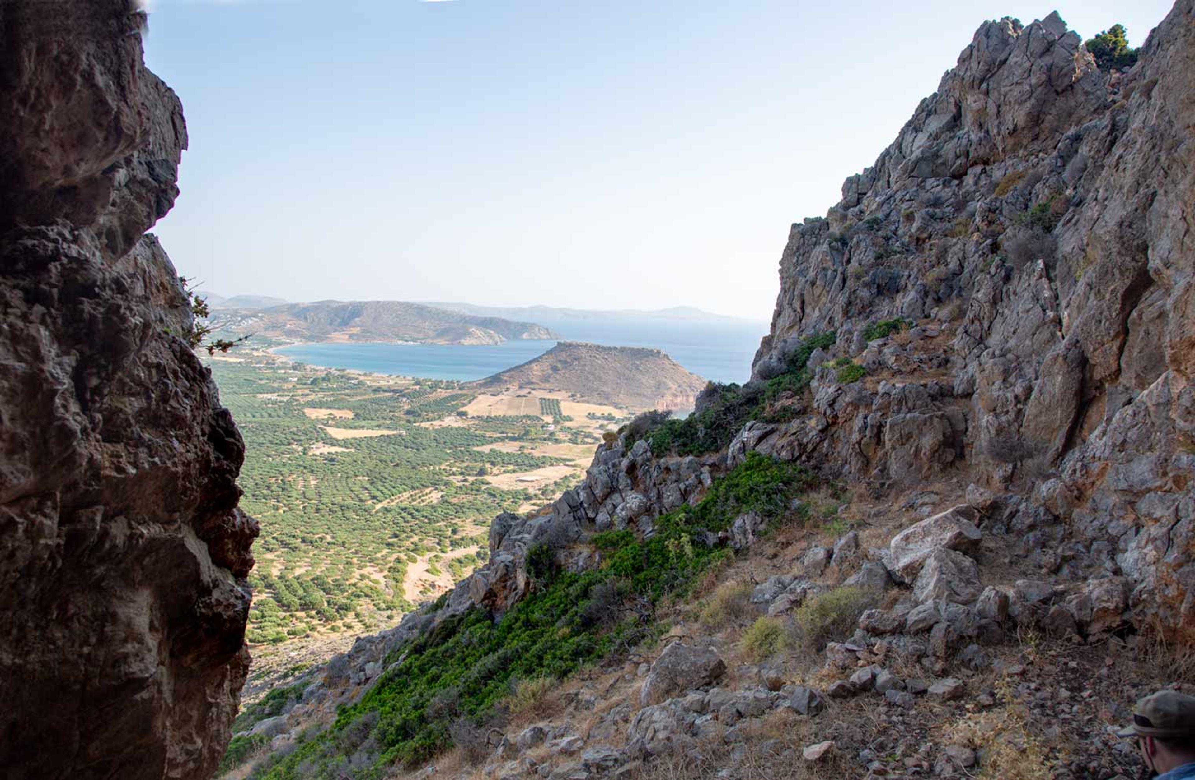 View from a mountain, looking through an opening in the rocks, overlooking an excavation site and the sea.