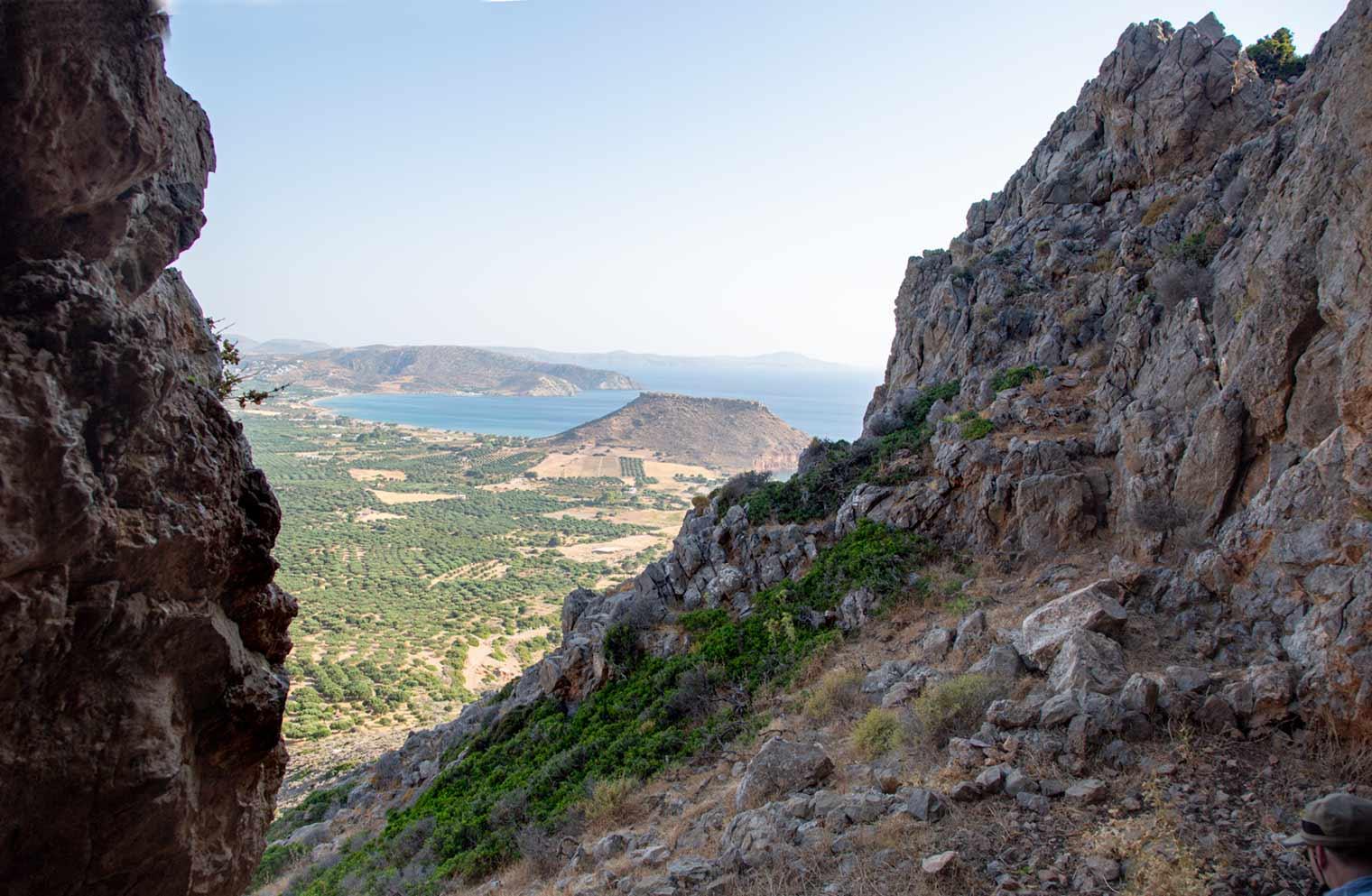 View from a mountain, looking through an opening in the rocks, overlooking an excavation site and the sea.