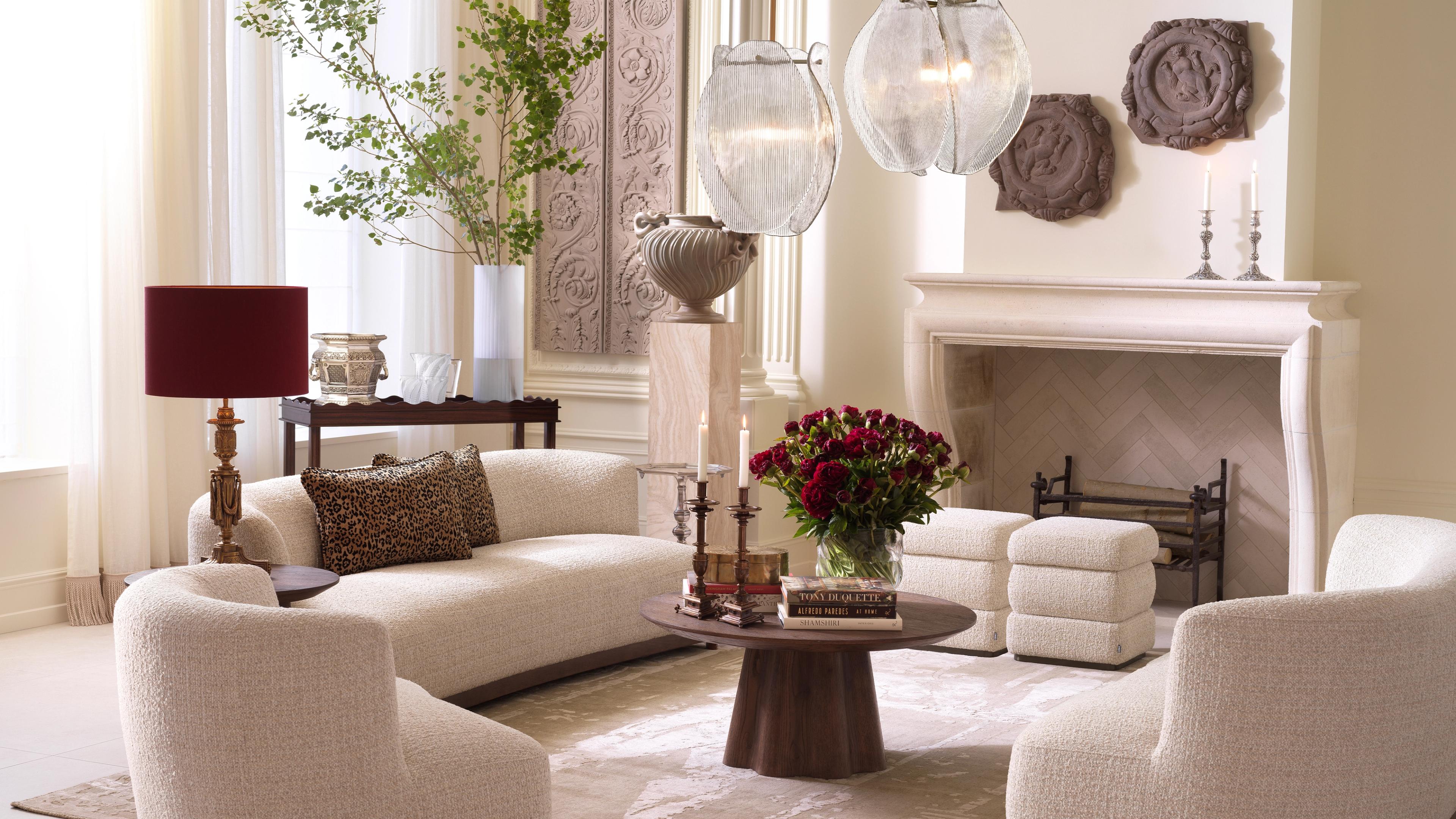 Warm and inviting living room featuring curved sofas, a round table with flowers, elegant lighting, and styled decor elements.