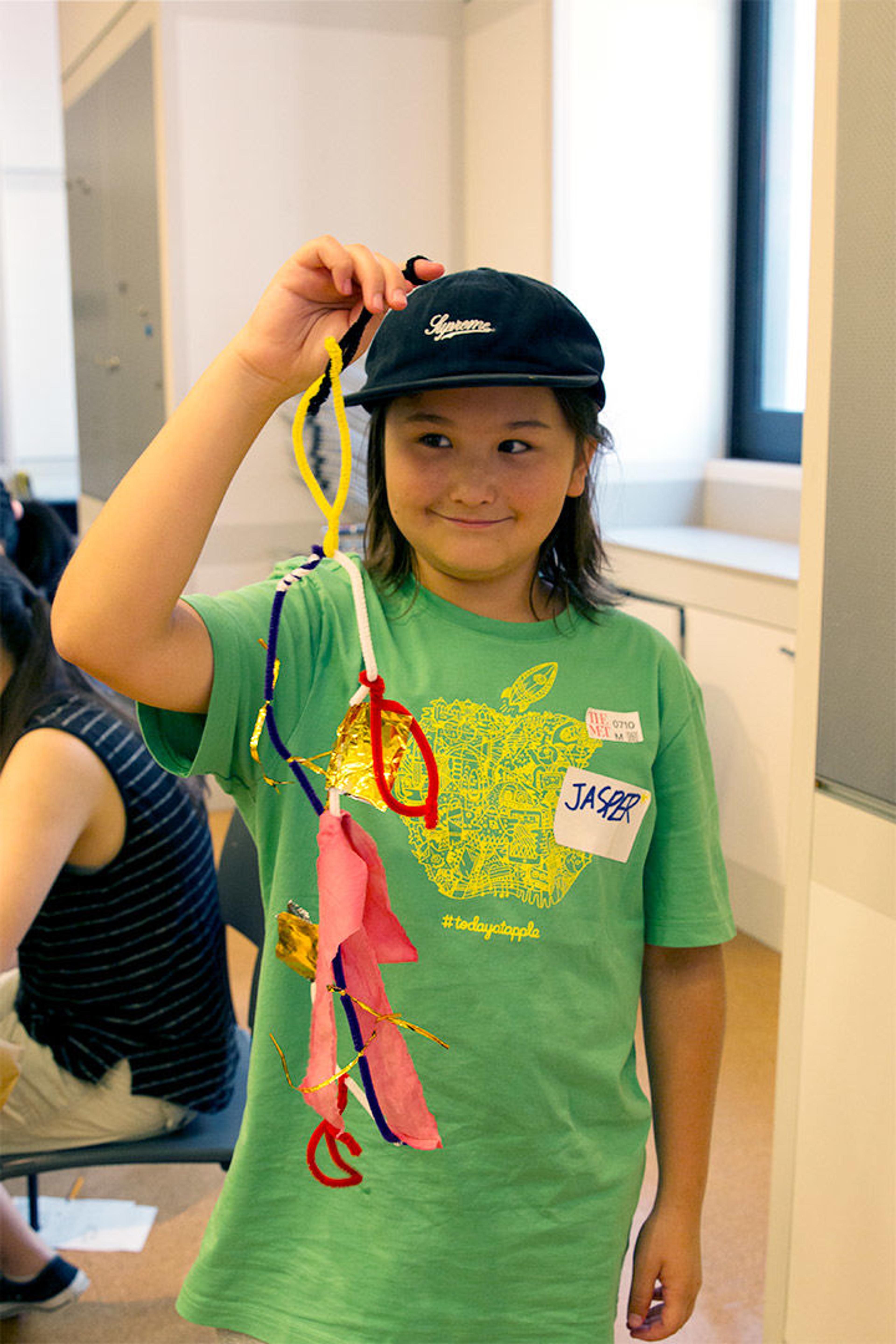 Jasper holds up his finished mobile made of dyed cloth, pipe cleaners, string, and other materials.