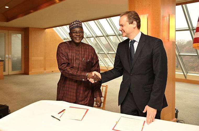 Two men standing in front of a desk shaking hands and smiling.
