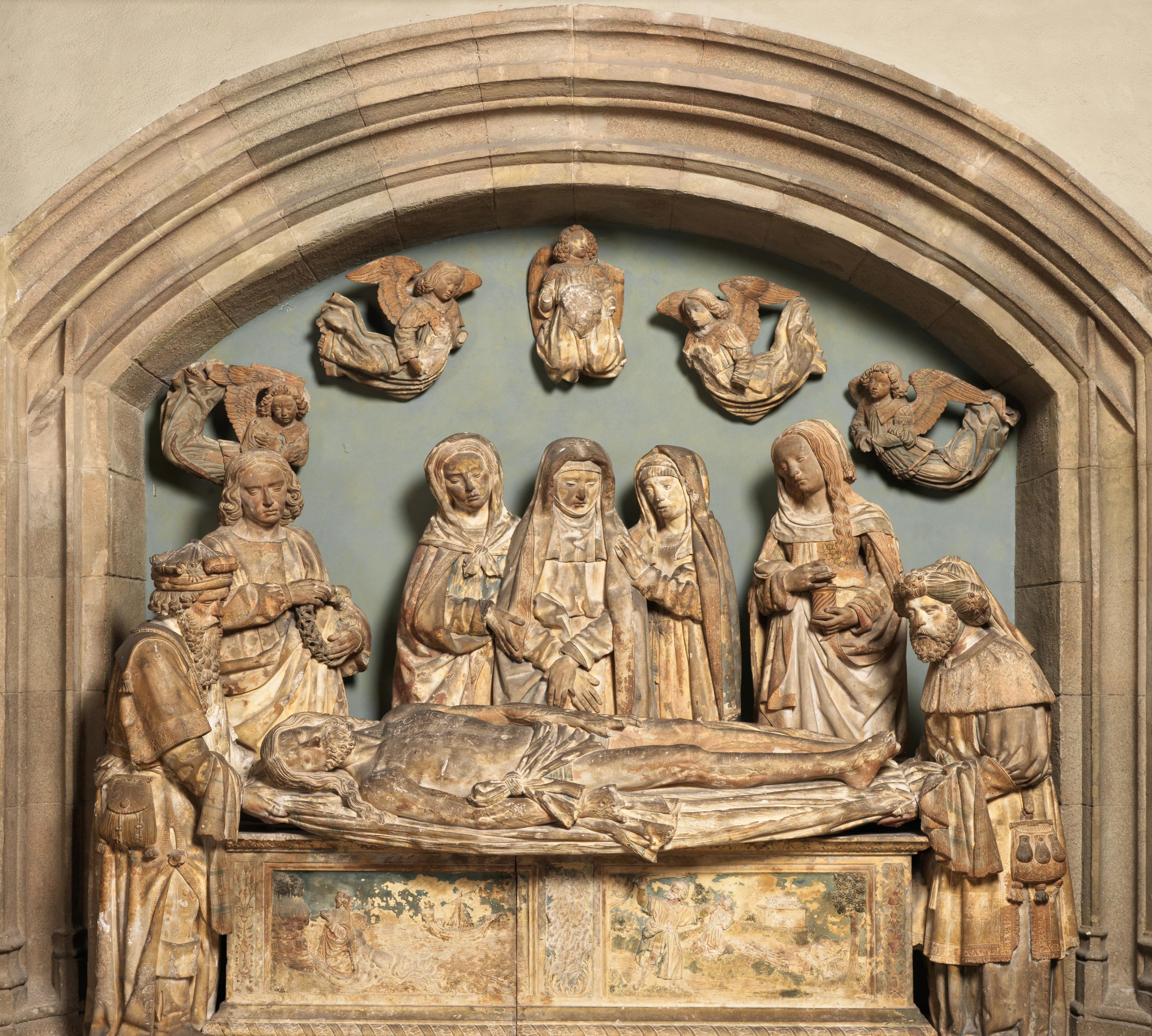 Sculptural scene showing seven figures assembled around the prone body of Christ atop a tomb. The piece shows significant discoloration throughout.