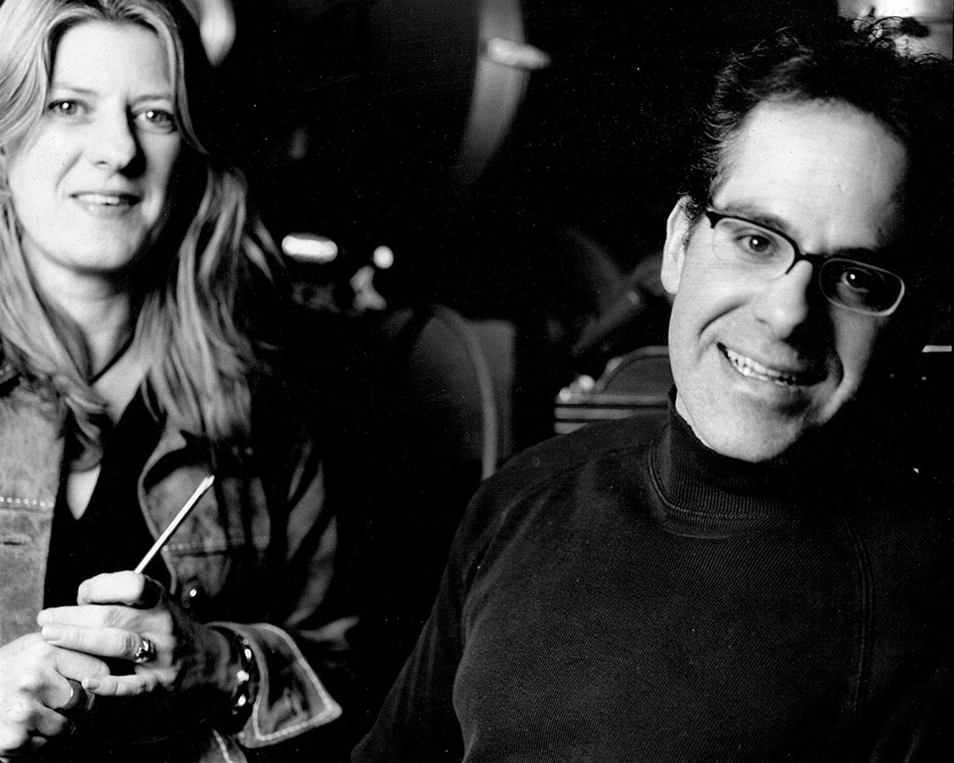 A woman holding a tool sits next to a smiling man wearing glasses in a black and white photo.
