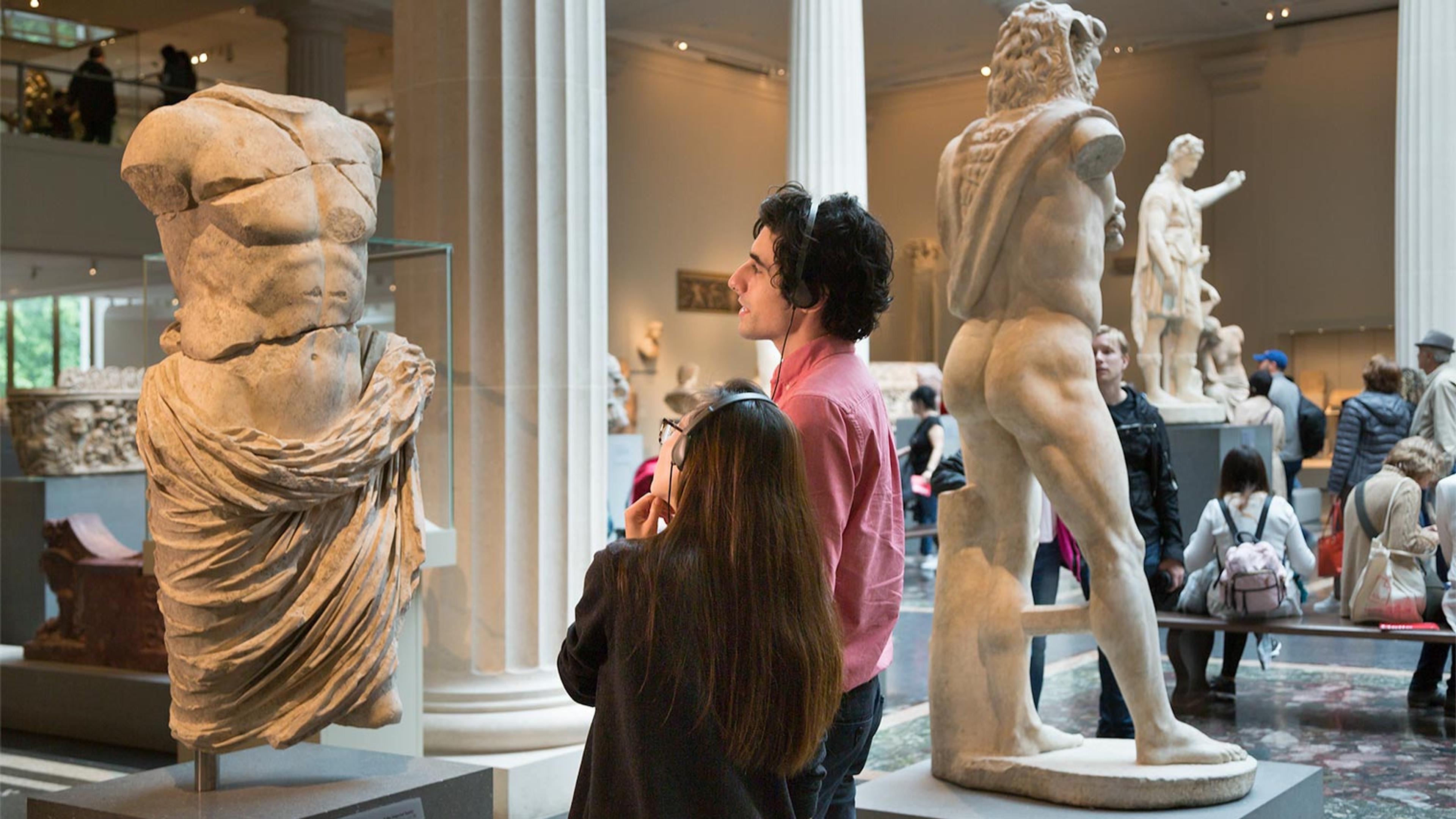 Two people with headphones stand in the Greek and Roman galleries