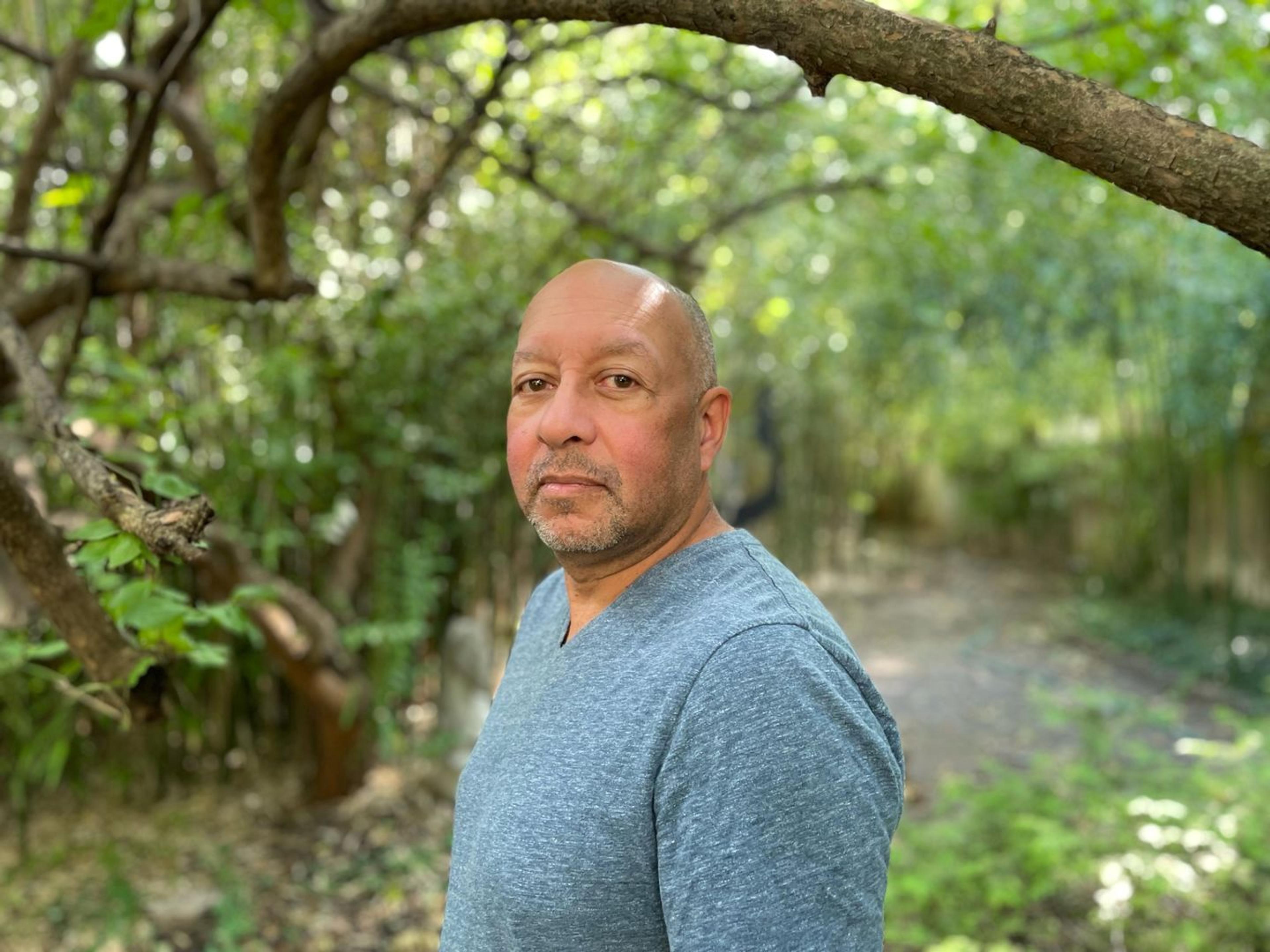 Man standing in the middle of the forest, wearing a grey shirt, looking at the camera