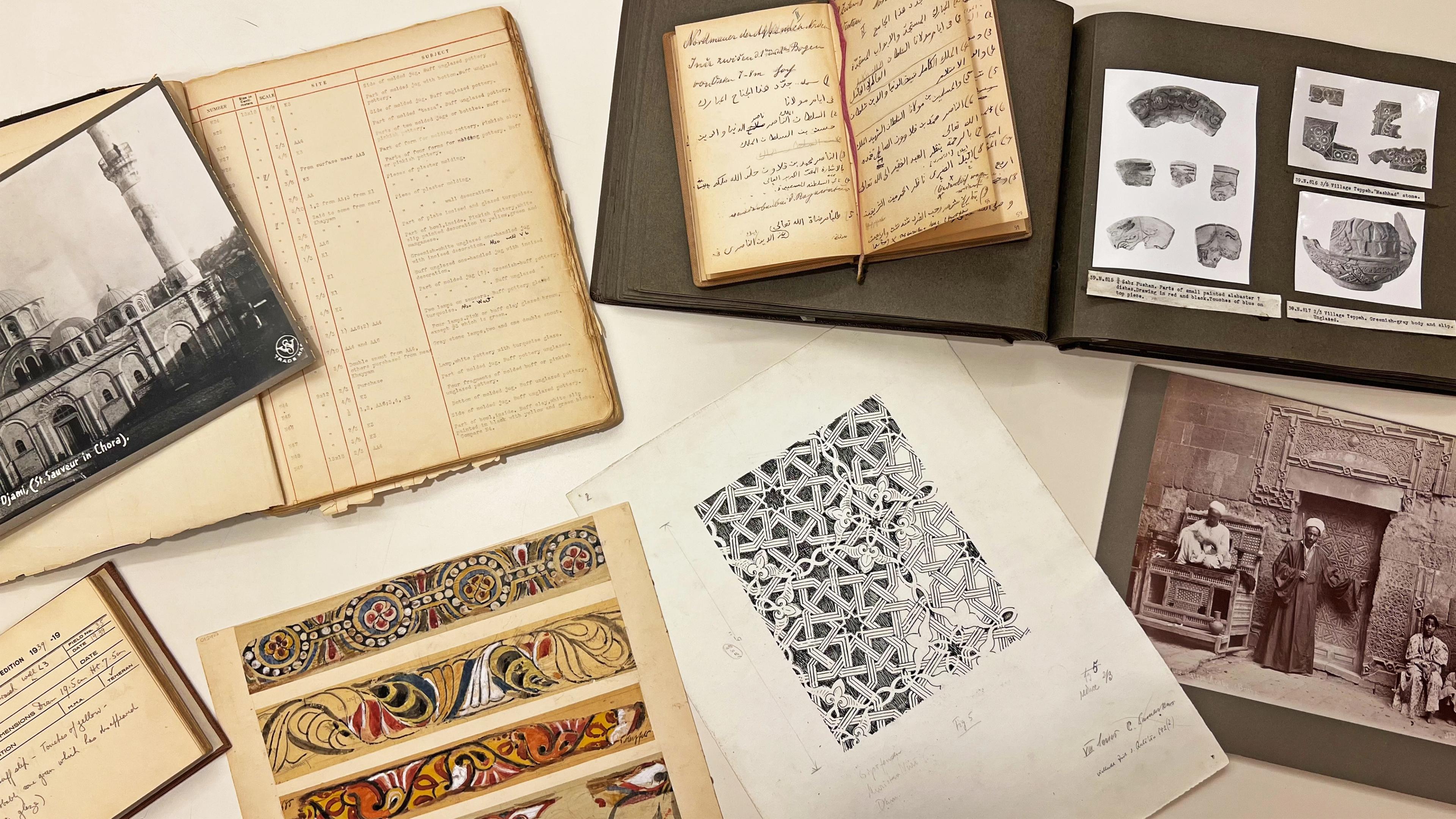 An assortment of archival materials such as notebooks, photographs and ink and watercolor studies on a table