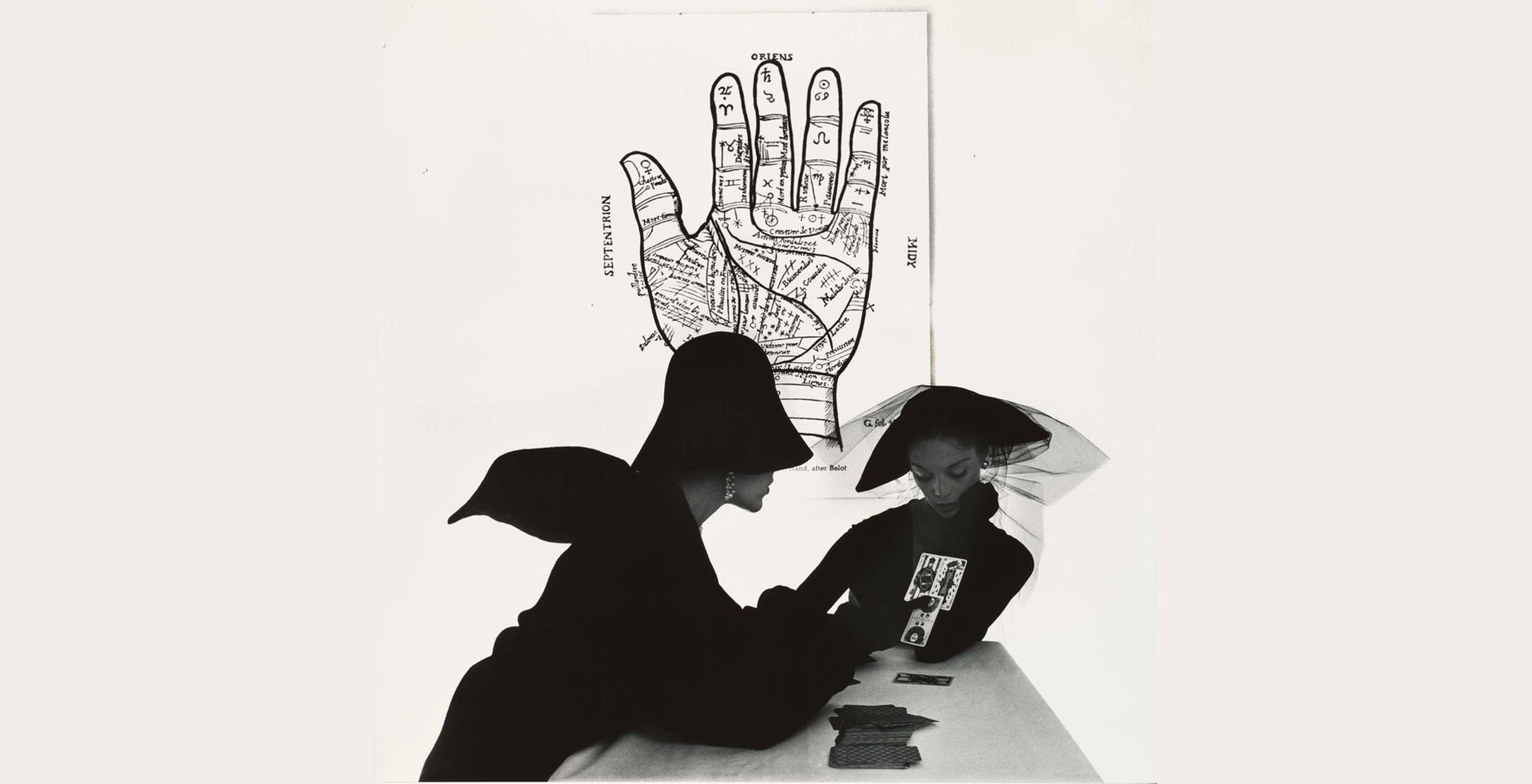 Irving Penn's "The Tarot Reader (Bridget Tichenor and Jean Patchett), New York" with two women in stylist black clothing reading tarot cards with a diagram of a hand behind them