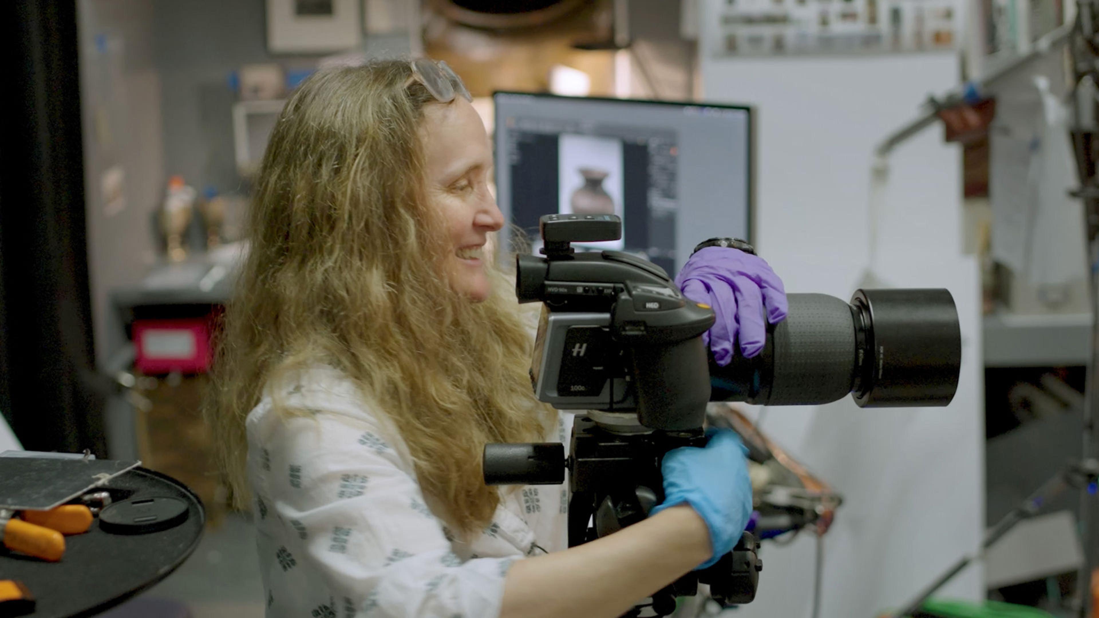 Photograph of photographer Eileen Travell smiling and adjusting a camera on a tripod.
