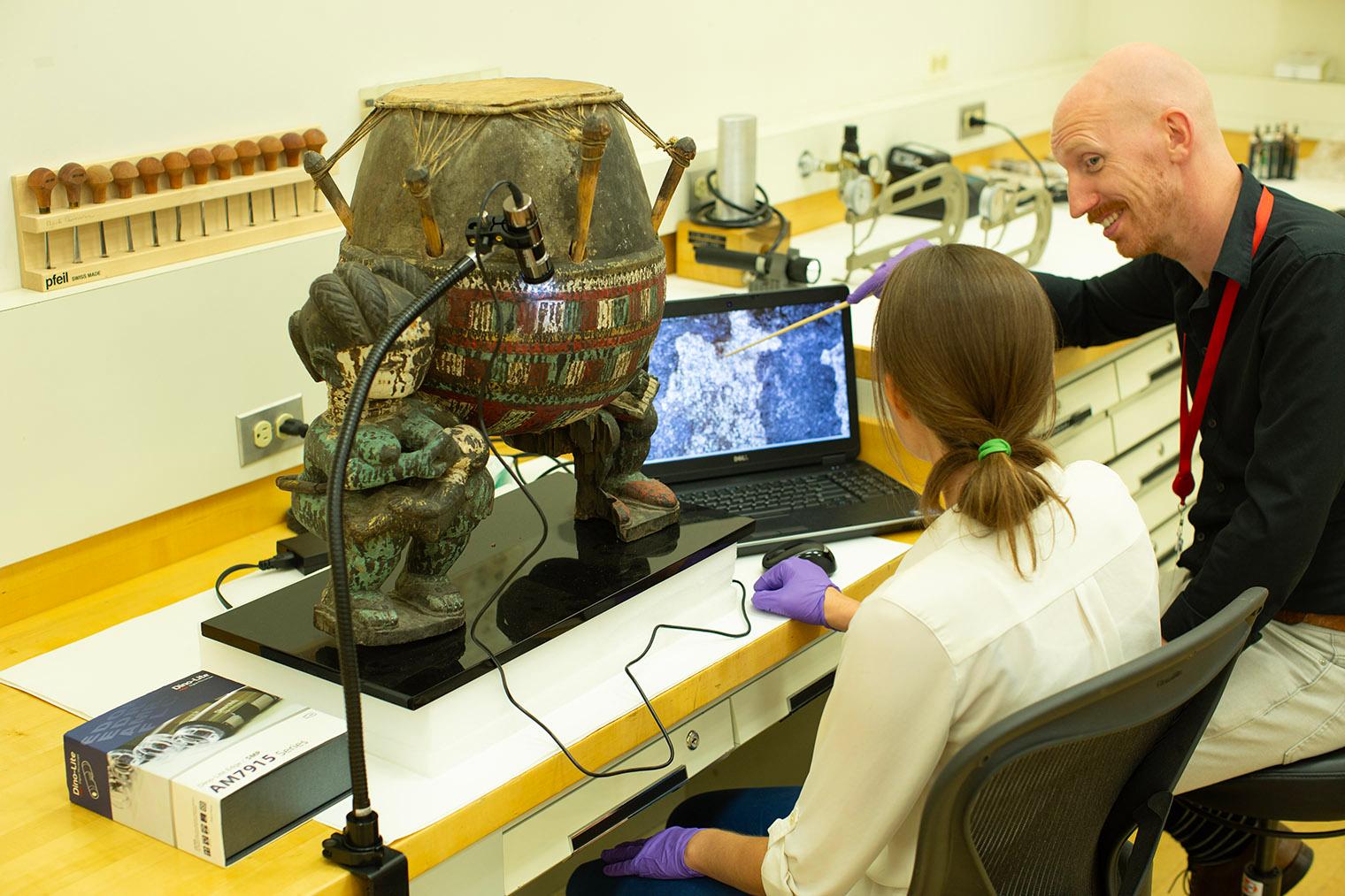 Two conservators looking at an African drum using microscopic technology.