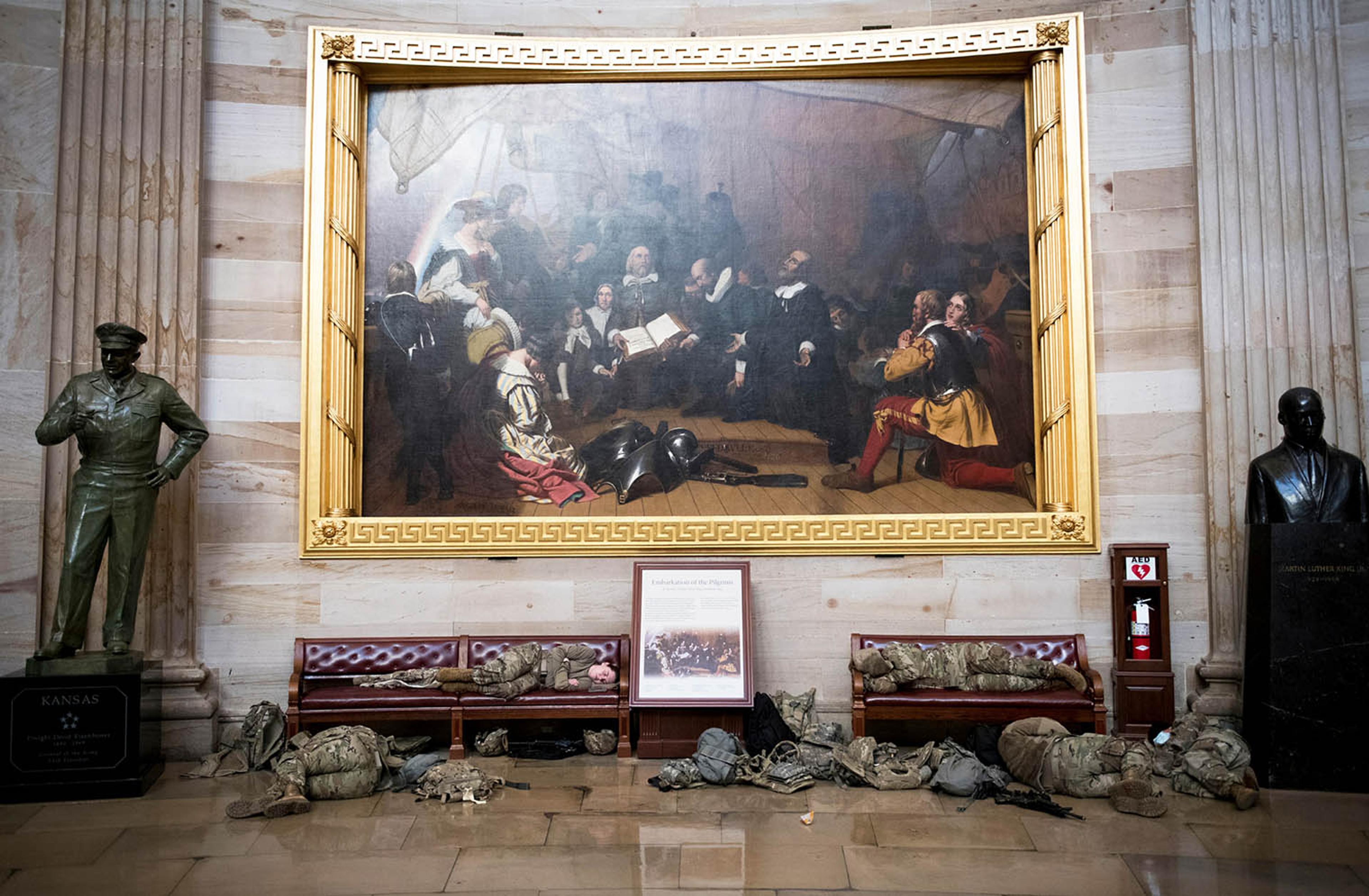 Soldiers sleeping in front of a large painting at the Capitol.
