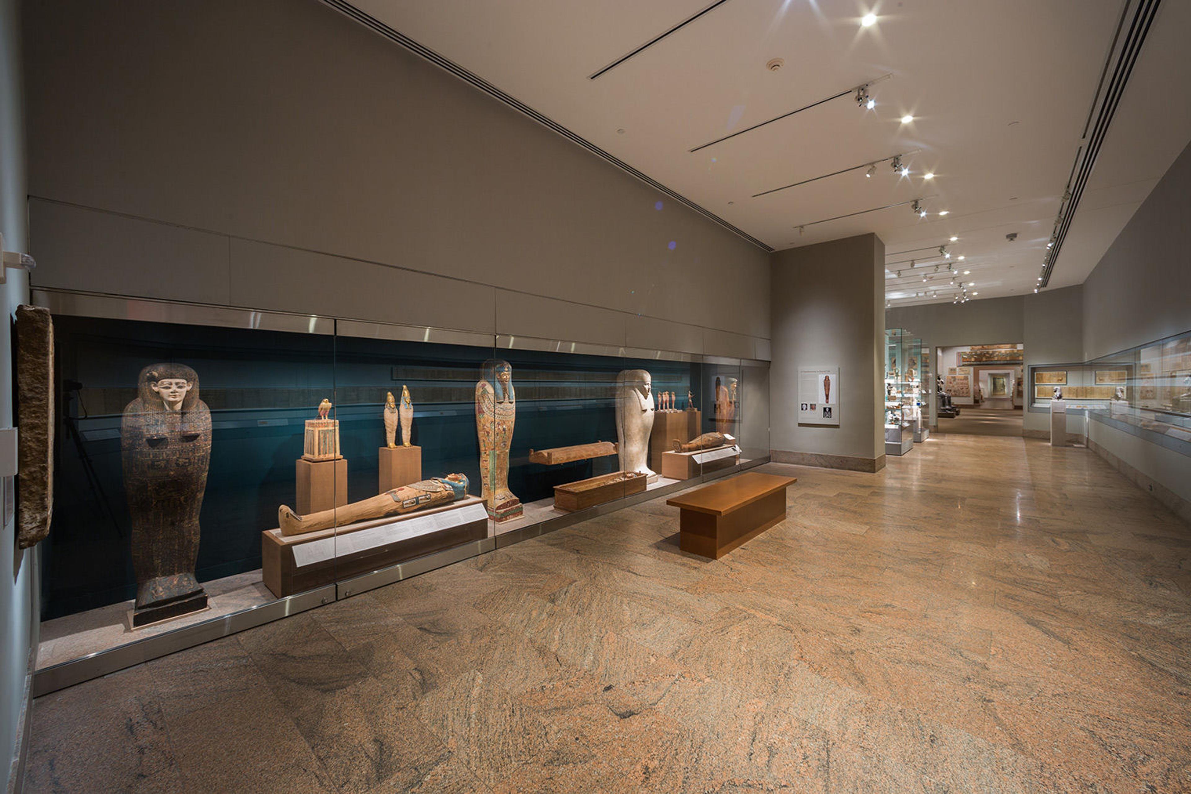 A view of the Ptolemaic galleries, with four standing coffins and two mummies lying down visible to the left.