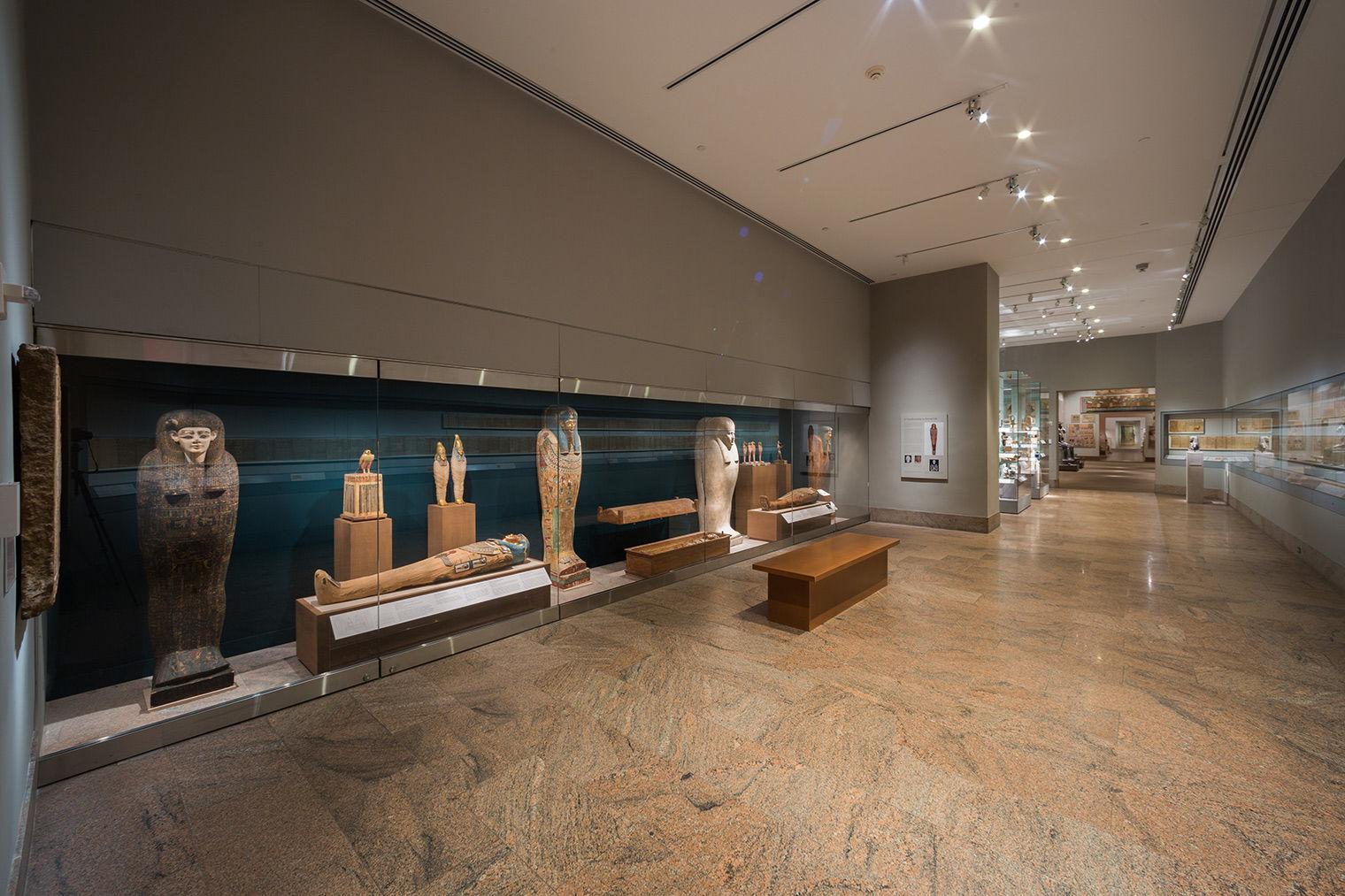 A view of the Ptolemaic galleries, with four standing coffins and two mummies lying down visible to the left.