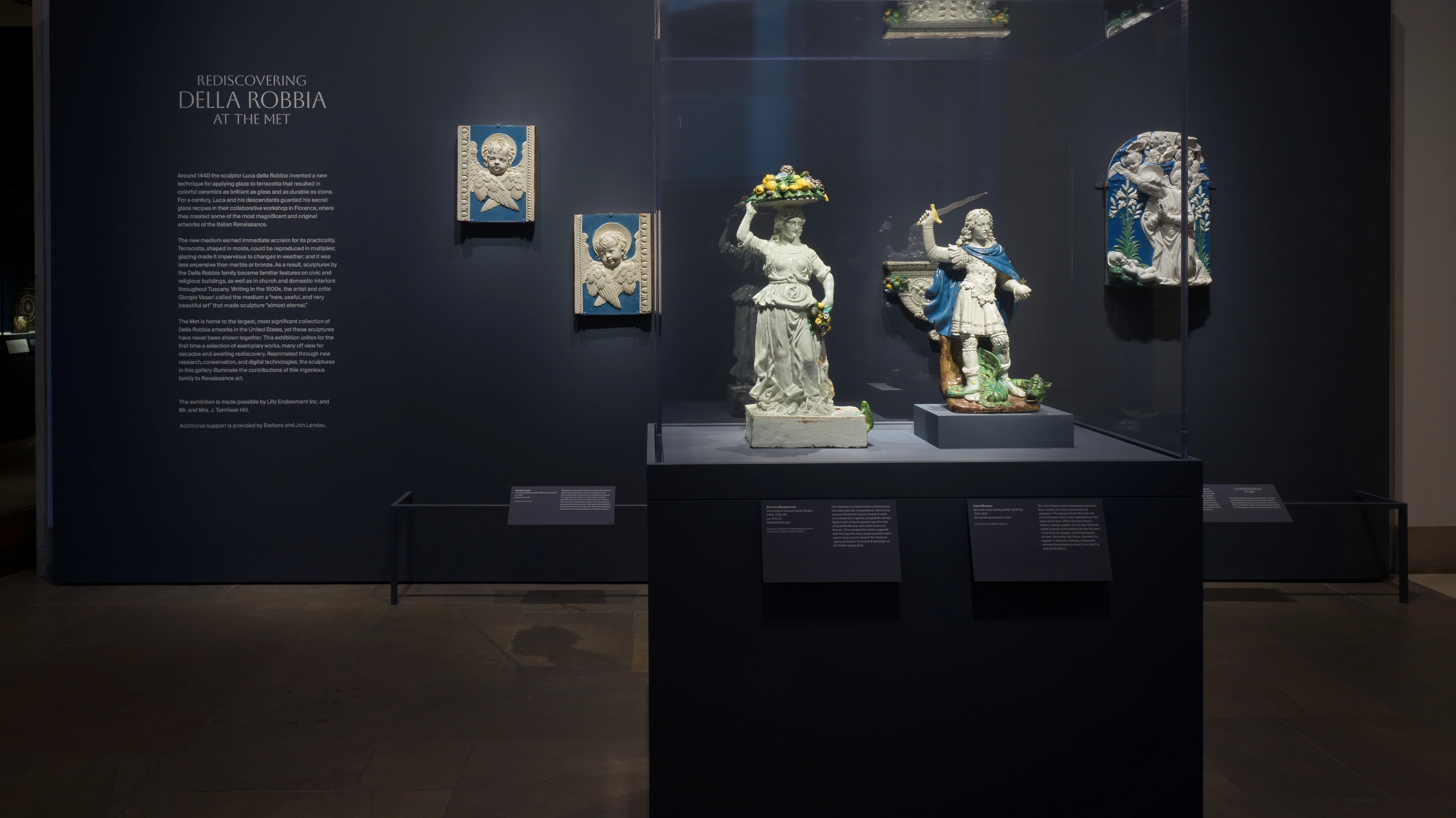 A dim museum gallery displays ornate porcelain figures and blue-and-white wall panels in glass cases.