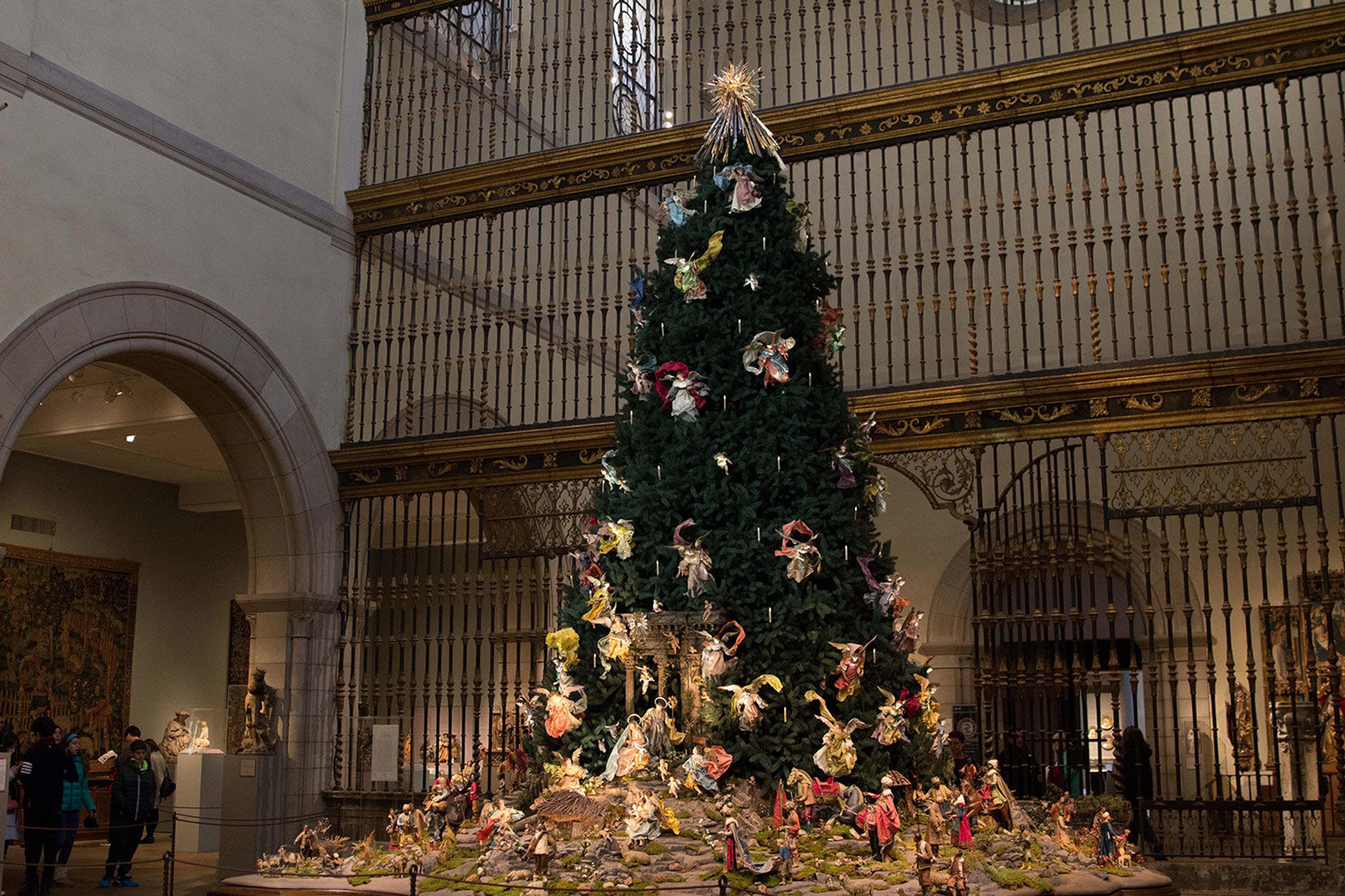 Picture of a dark green Christmas tree display with colorful ornaments and golden accents in the museum.